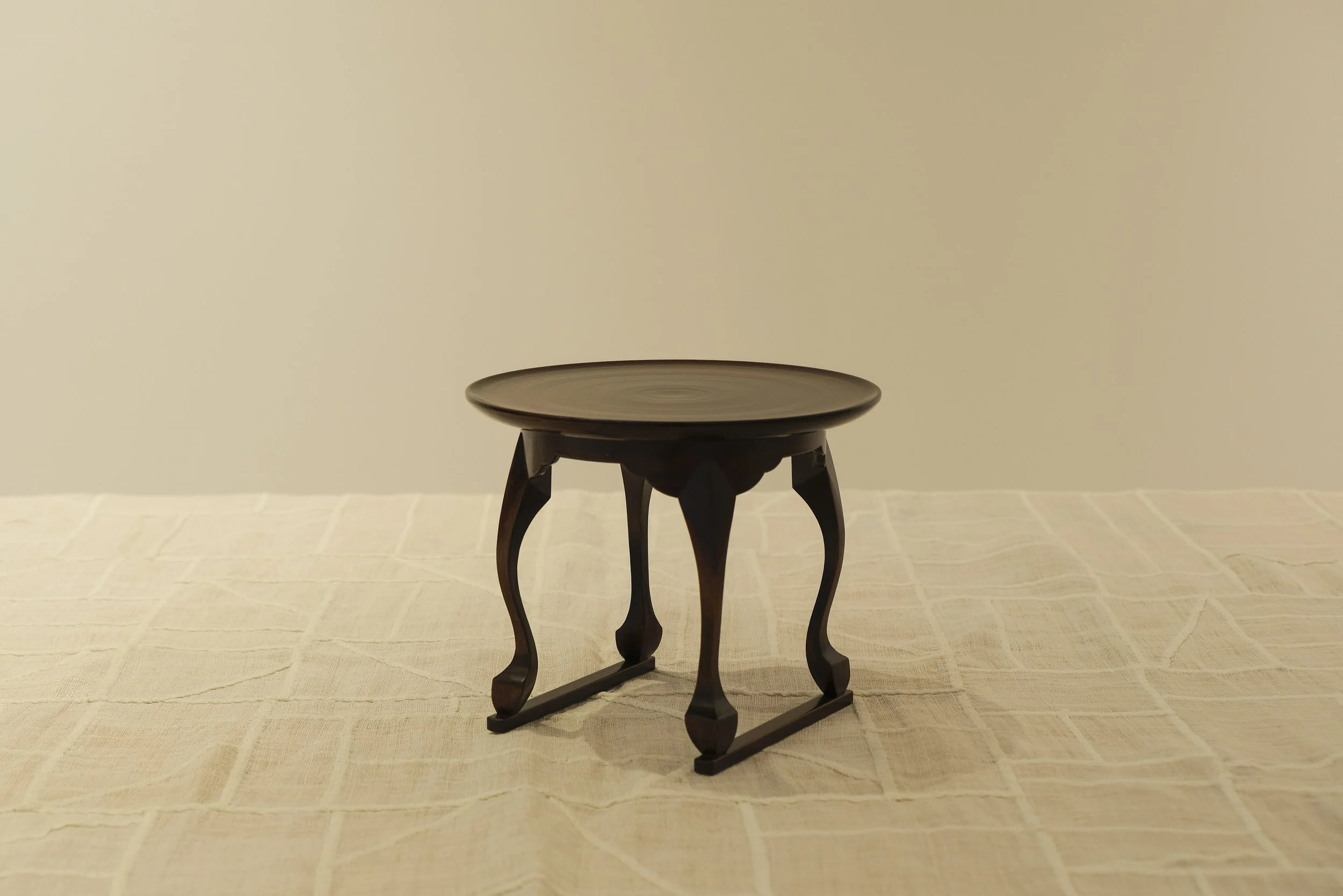 Small wooden table with curved legs on a beige tablecloth against a plain light-colored wall.