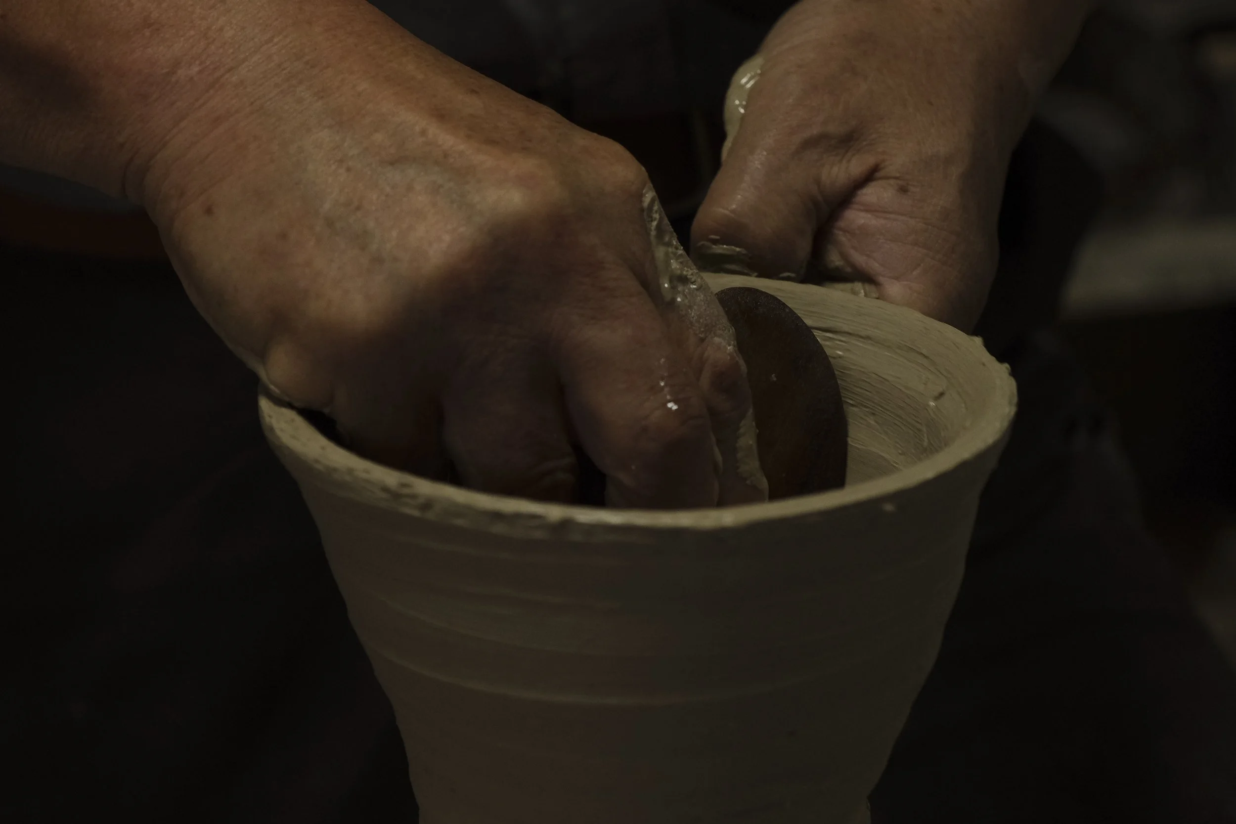 Hands shaping clay on a pottery wheel to form a cup or vessel.