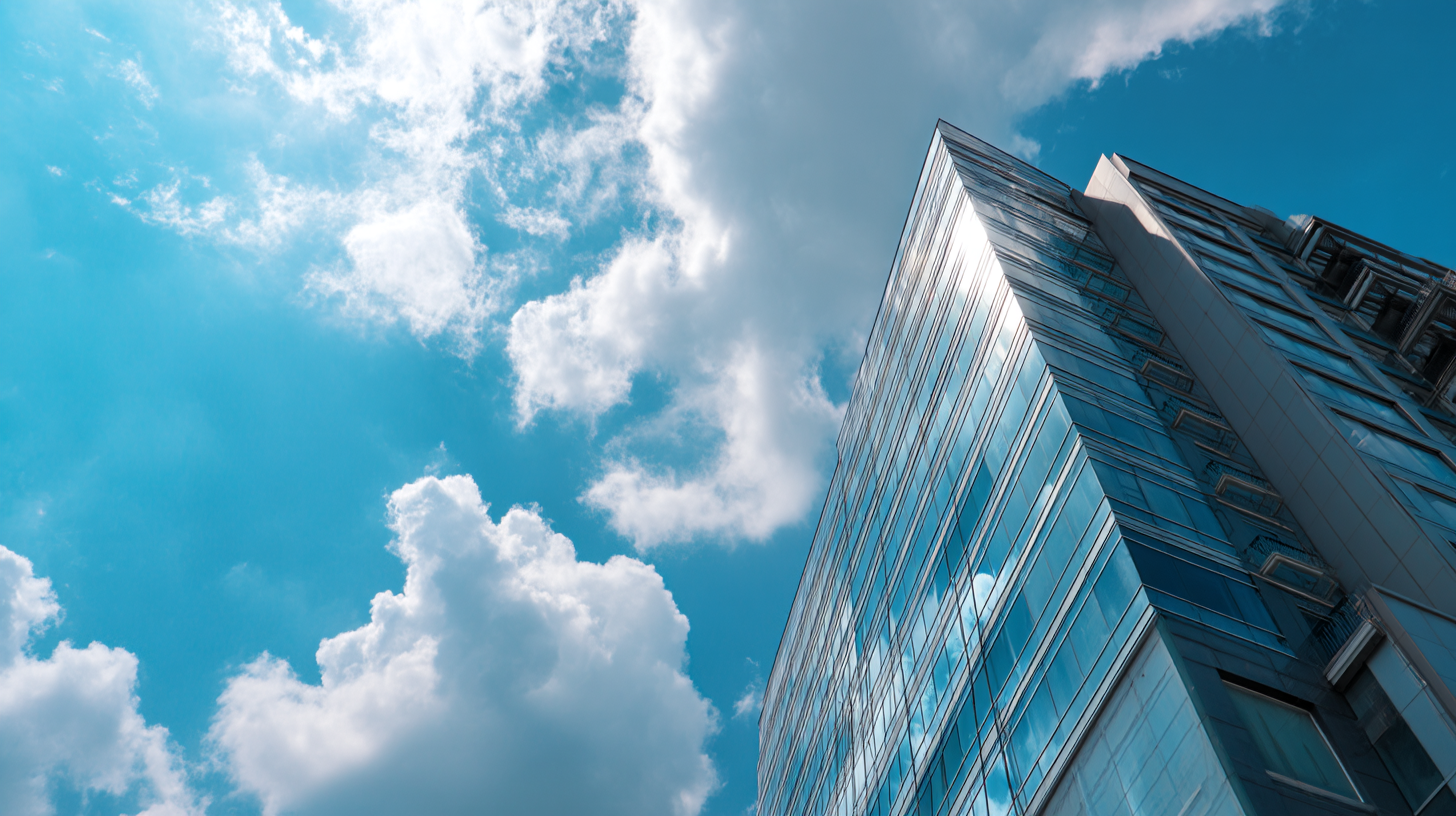 Low-angle view of a modern glass skyscraper reflecting clouds and the blue sky