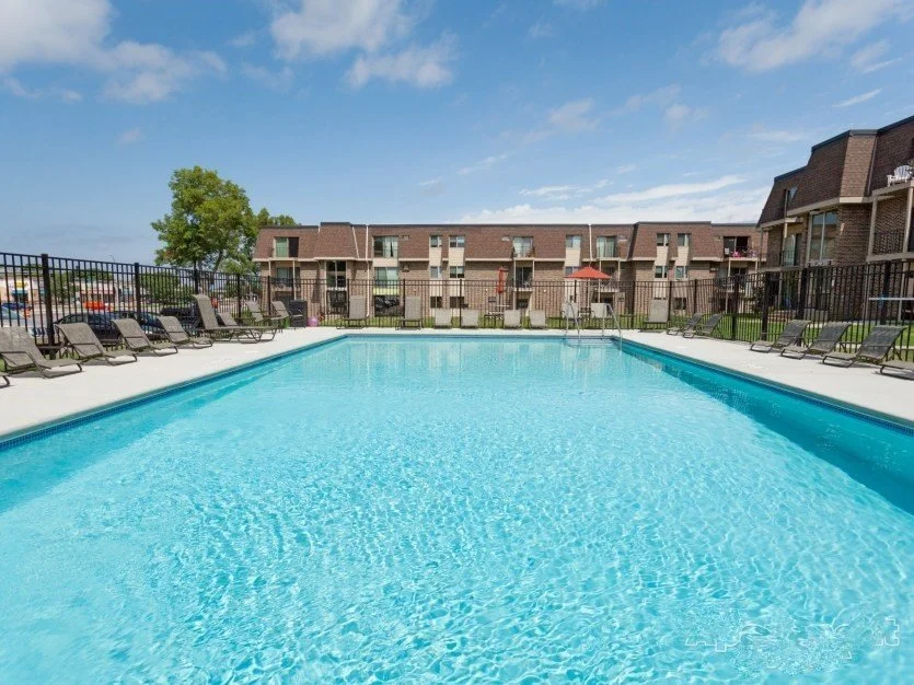 Outdoor swimming pool with lounge chairs, surrounded by a black metal fence, River Ridge apartments.