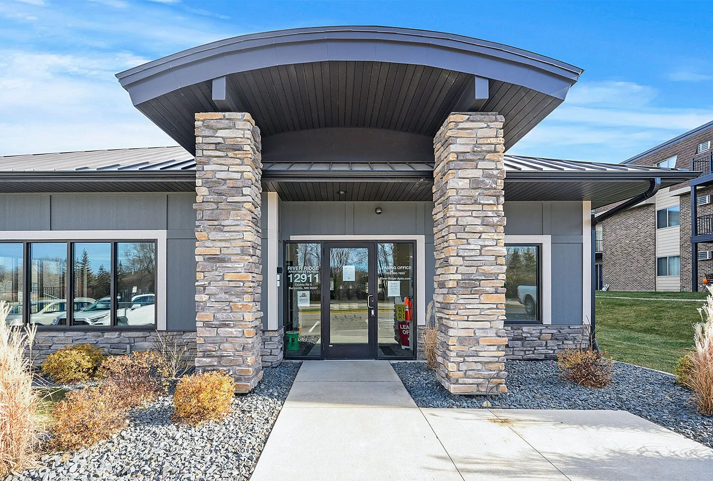 Front entrance of River Ridge apartment leasing office with stone pillars, glass doors, and large windows
