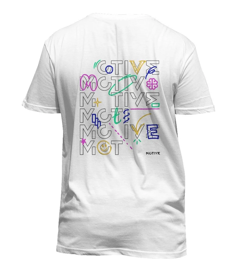 White t-shirt with colorful, abstract text and symbols. The design includes the logo 'MOTIVE' with various letters and doodles in different colours like pink, green, blue, and yellow.