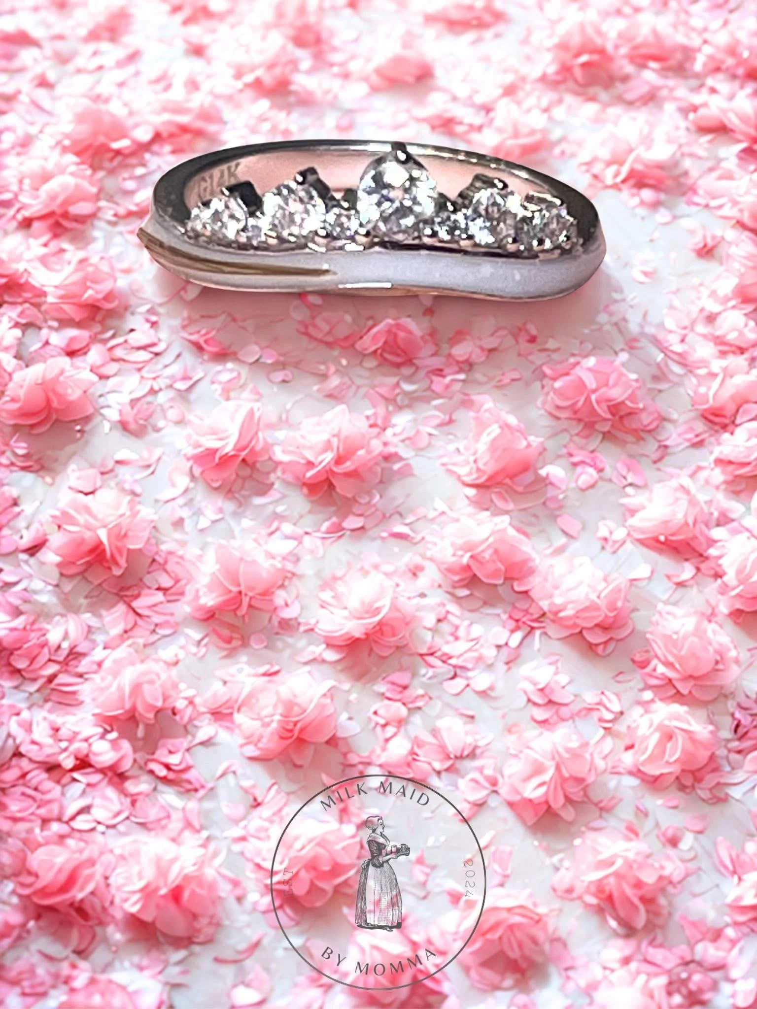 A silver ring with a heart-shaped center stone surrounded by small diamonds, placed on a grey surface.