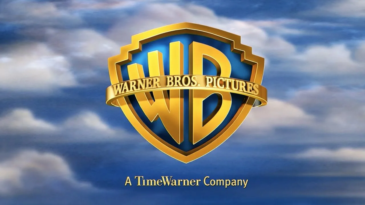 The Warner Bros. Pictures logo featuring a gold shield with the initials WB in the center, set against a cloudy sky background, with a banner across it reading "WARNER BROS. PICTURES" and text below stating "A TimeWarner Company."