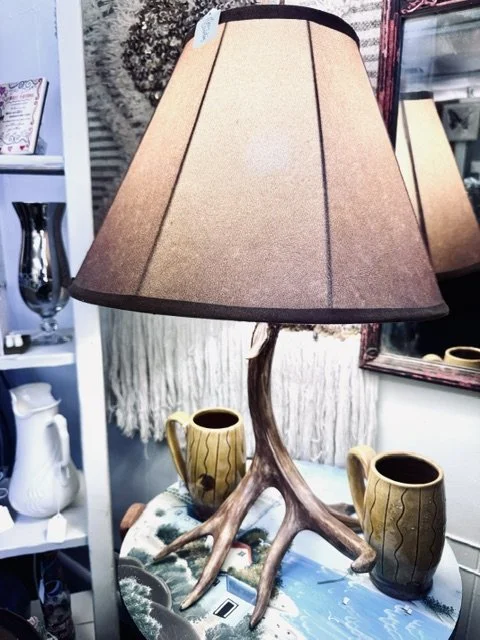 Table lamp with a lampshade, a base designed to look like tree branches, placed on a table with two yellow vases, a mirror, and decorative items in a home decor store.