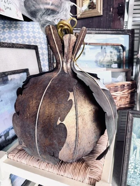 Rusty metal pumpkin sculpture with dolphin cutouts, placed on a wicker basket with picture frames in the background.