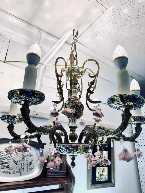 A vintage chandelier with floral and bell-shaped hanging decorations in a room with white ceilings.