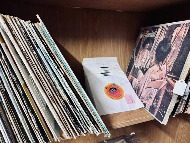 A bookshelf with magazines and vinyl records, including a record with a pink sticker and a pink note.