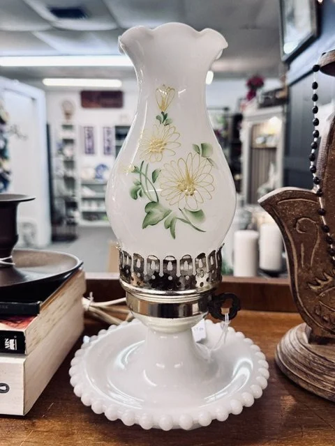 Decorative ceramic oil lamp with floral design on a wooden table in a thrift store or antique shop.