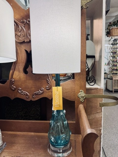 Table lamp with a white shade and a blue-green glass base on a wooden table.