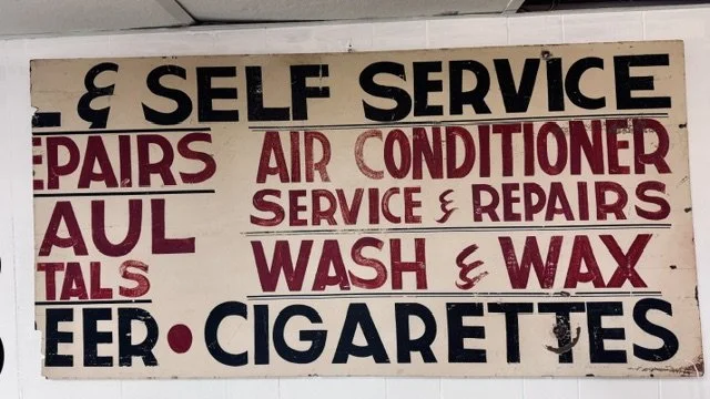 Sign advertising self-service car repairs, air conditioning service and repairs, wash and wax, and cigarettes.