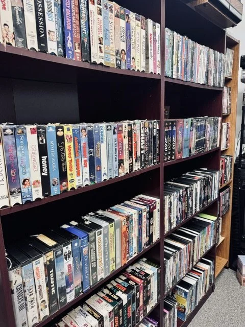 Bookshelves filled with VHS tapes arranged vertically and horizontally in a store or library.