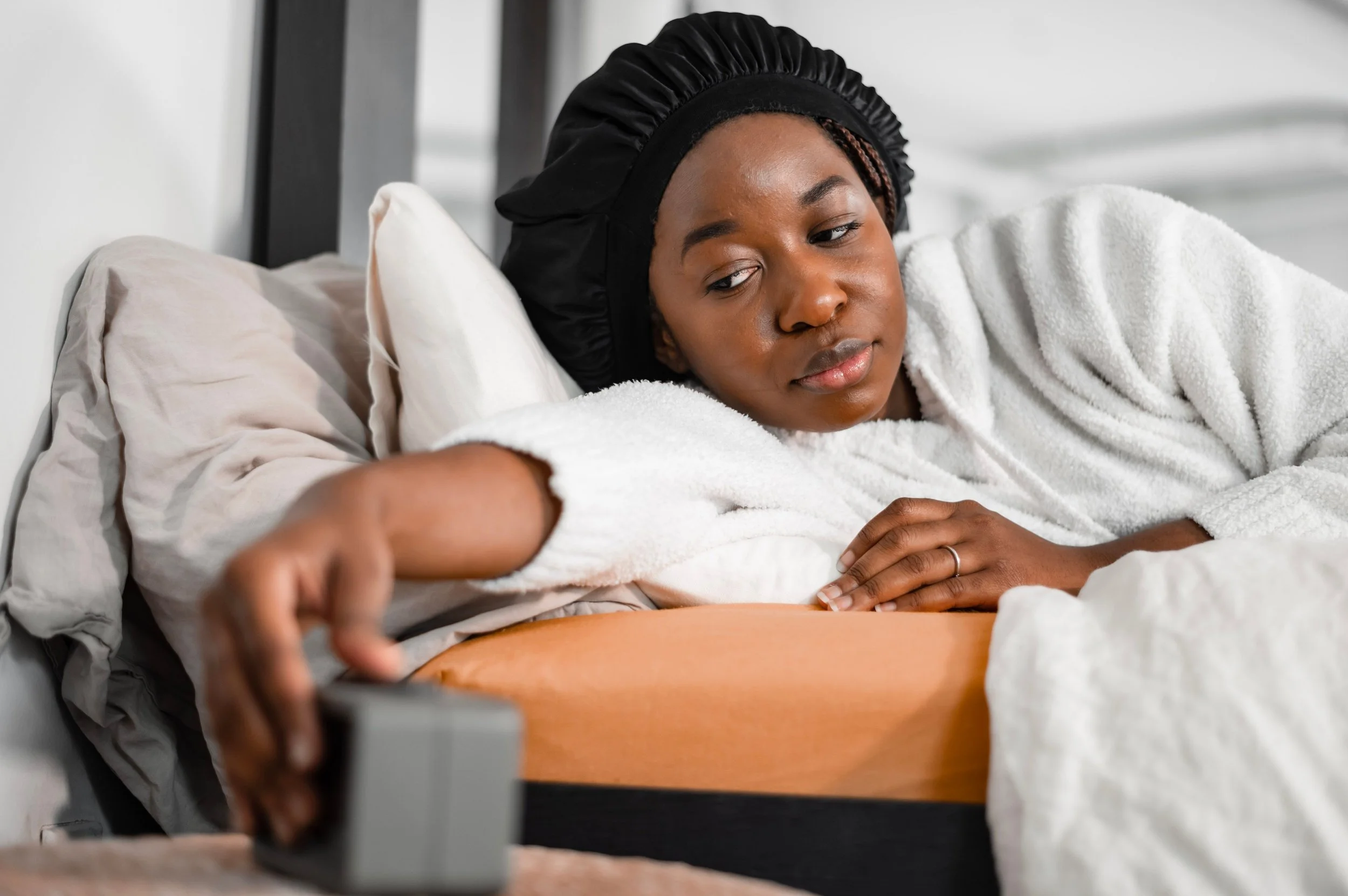 Woman lying awake in bed reaching toward a bedside alarm clock