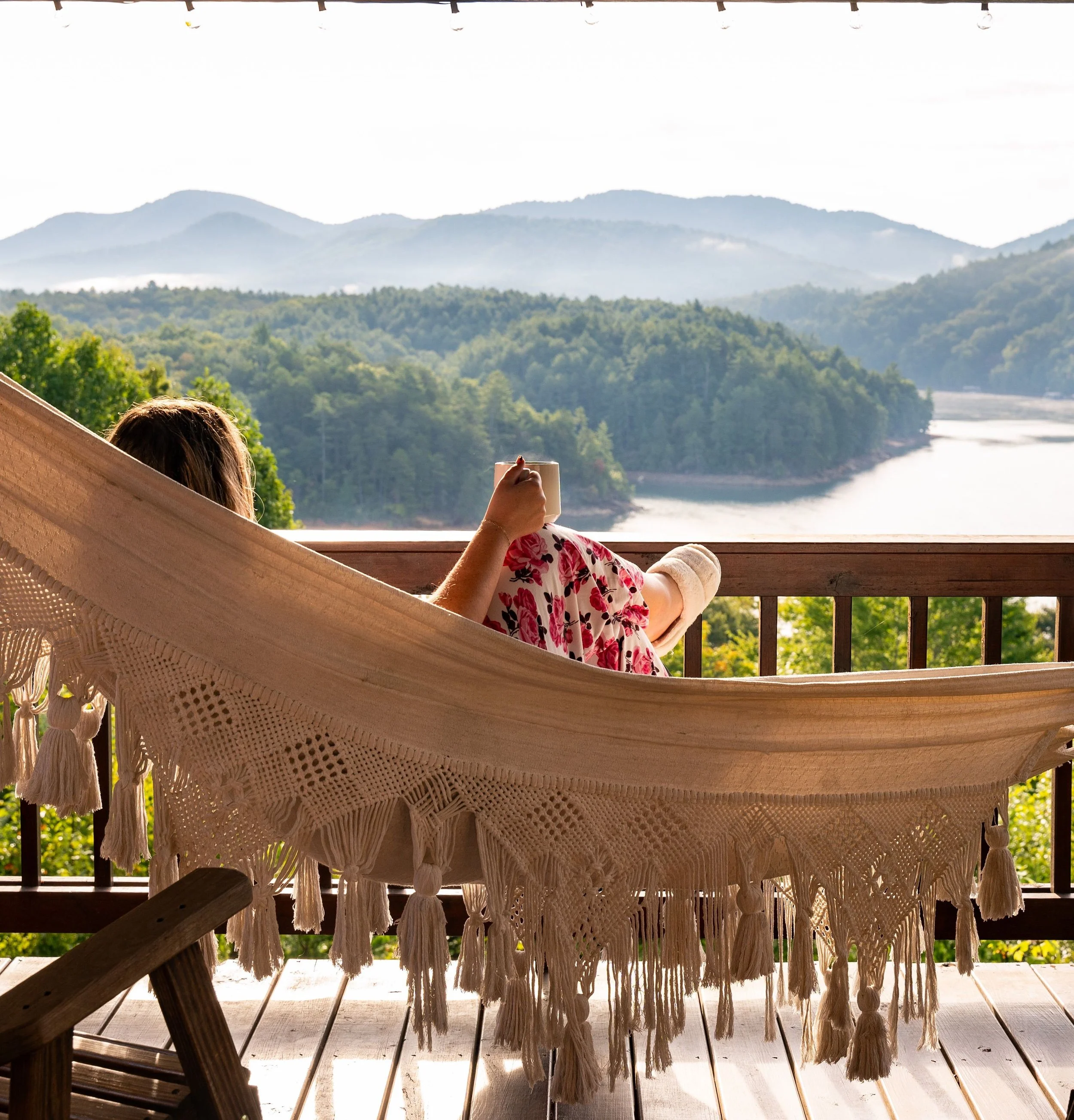 Person relaxing in a hammock with a cup of coffee overlooking a peaceful mountain lake while reflecting on why a good moment doesn't always feel like enough.
