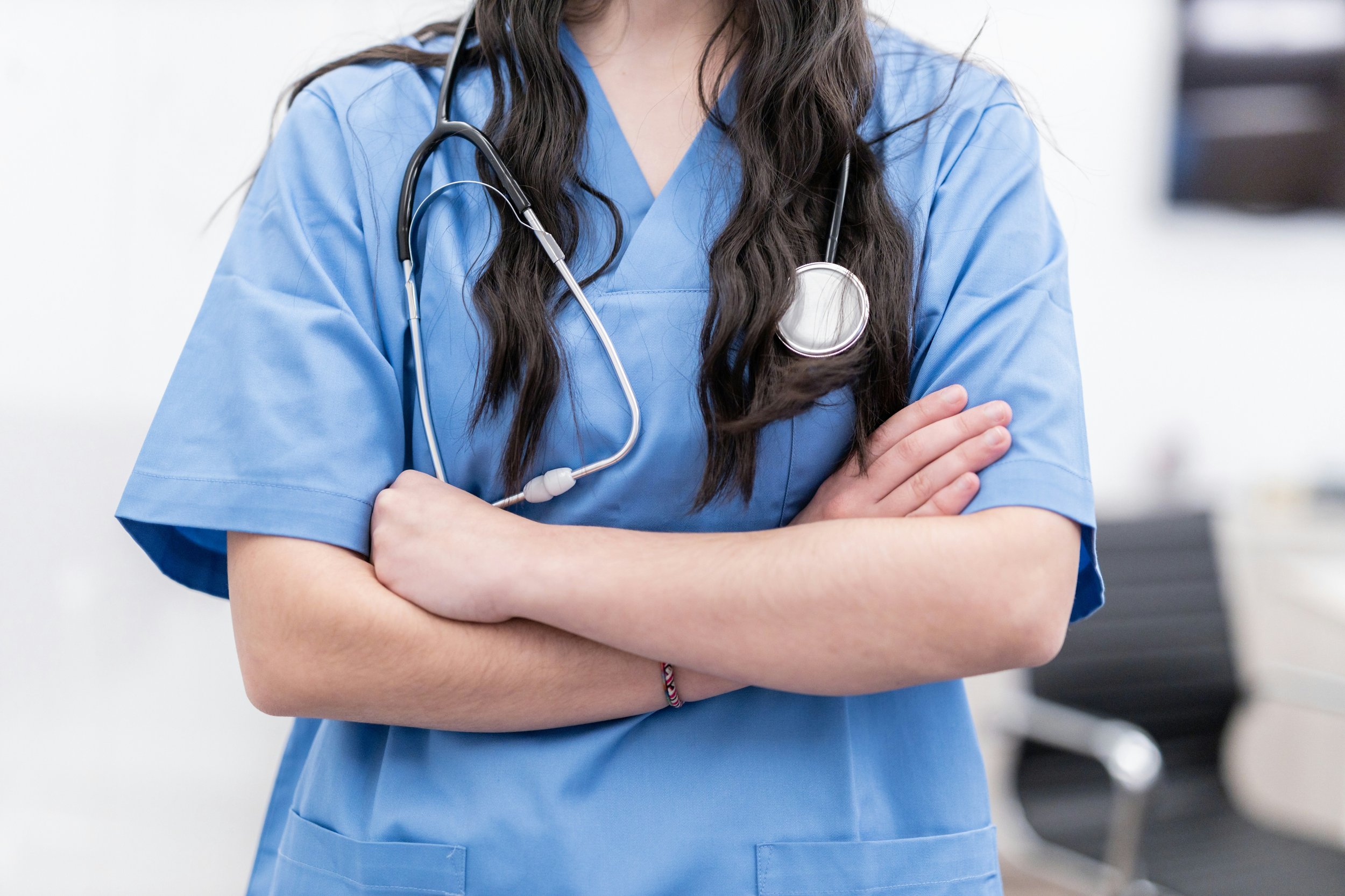 Person in blue medical scrubs with a stethoscope, arms crossed.