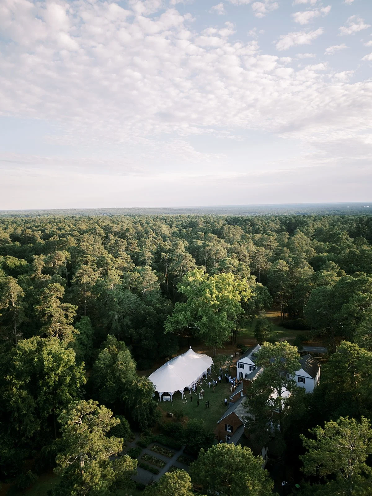 High aerial drone view of a white sailcloth tented wedding reception on a secluded wooded estate in New England, designed and coordinated by Carolyn Touchette Events.