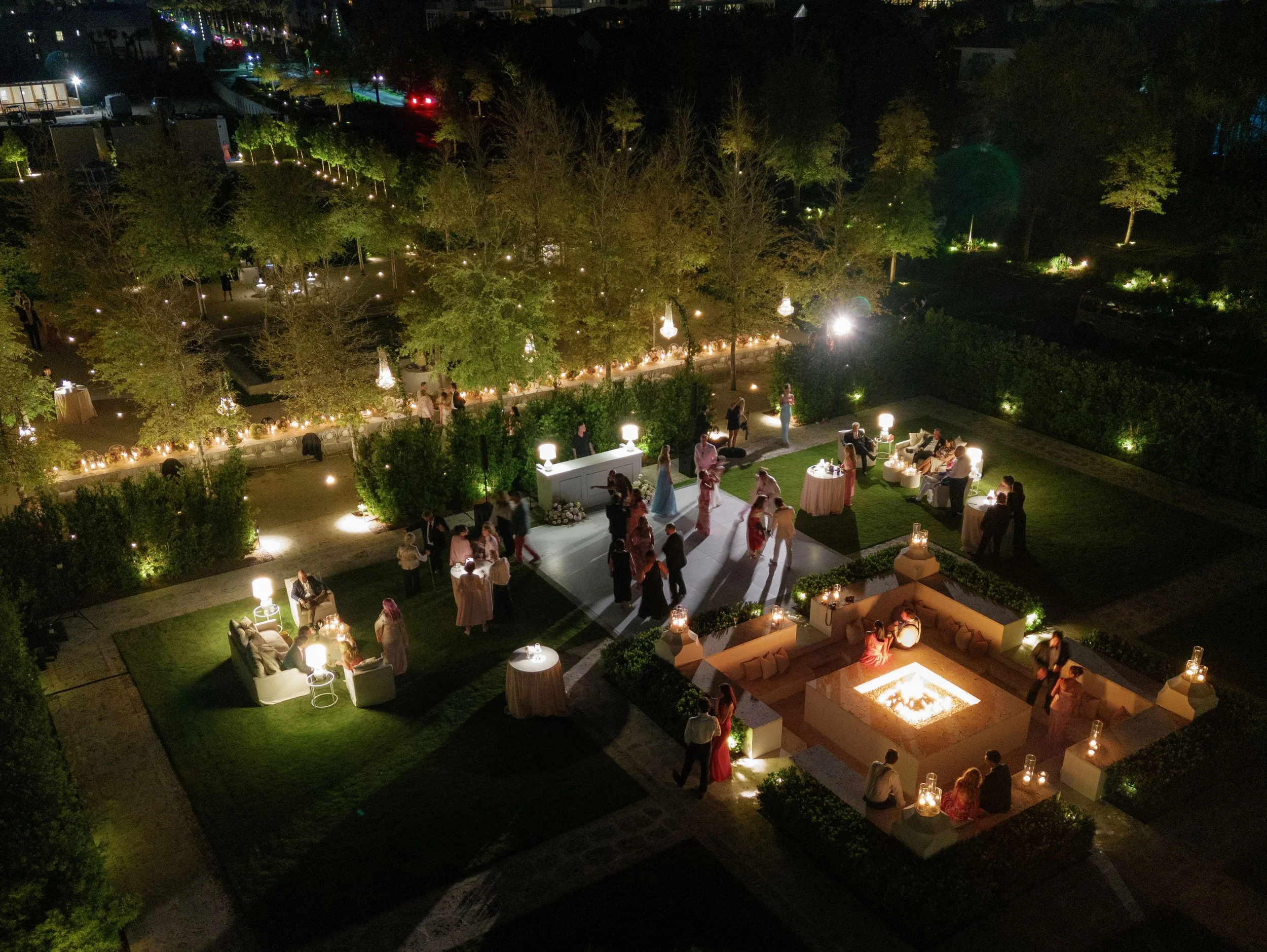 Aerial night view of a luxury outdoor wedding reception courtyard with custom ambient lighting, white dance floor, lounge seating, and guests dancing, planned by Carolyn Touchette Events in Rosemary Beach, Florida.