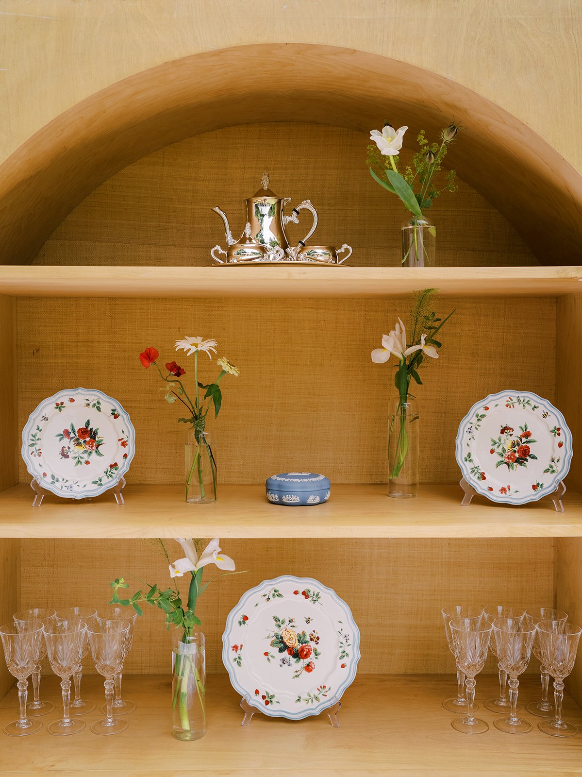 Stylized display shelf with vintage floral plates, delicate glass bud vases, crystal glassware, and heirloom silver tea set, designed by Carolyn Touchette Events.