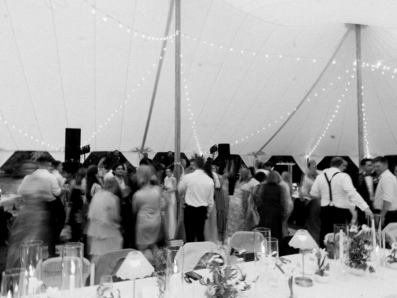 Black and white candid photo of wedding guests dancing on a crowded dance floor under a sailcloth tent with glowing string lights, by Carolyn Touchette Events.