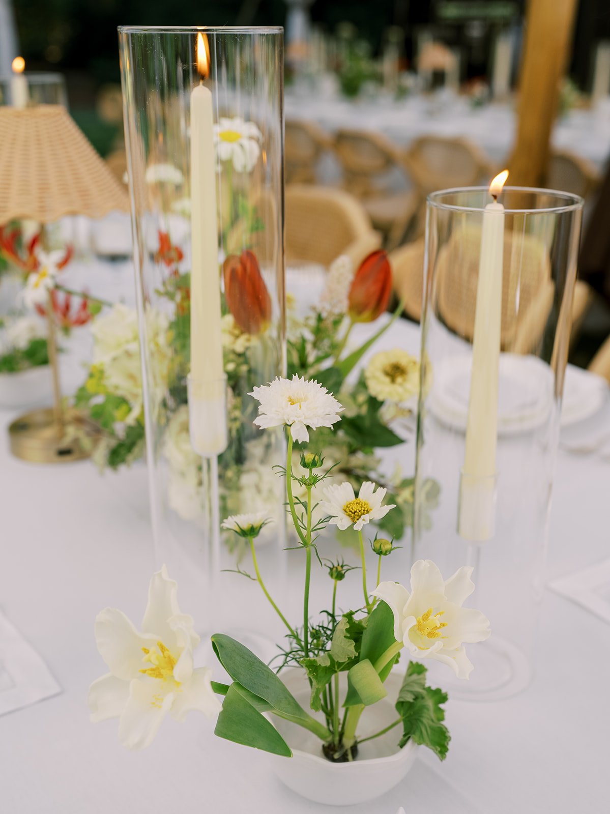 Detail shot of a cordless rattan table lamp and delicate white cosmos centerpiece providing warm ambient light for an intimate night reception dinner by Carolyn Touchette Events.