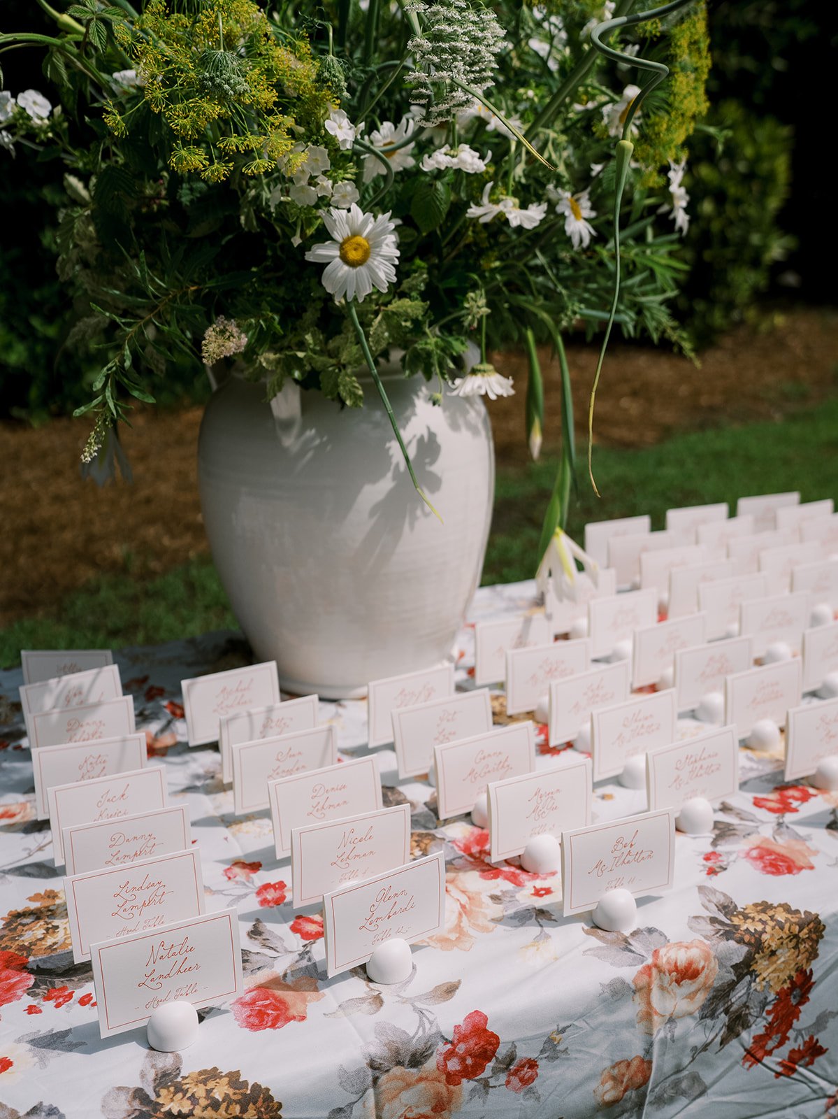 Elegantly arranged wedding escort cards with calligraphy on a vintage floral tablecloth alongside a large organic garden floral arrangement, designed by Carolyn Touchette Events.