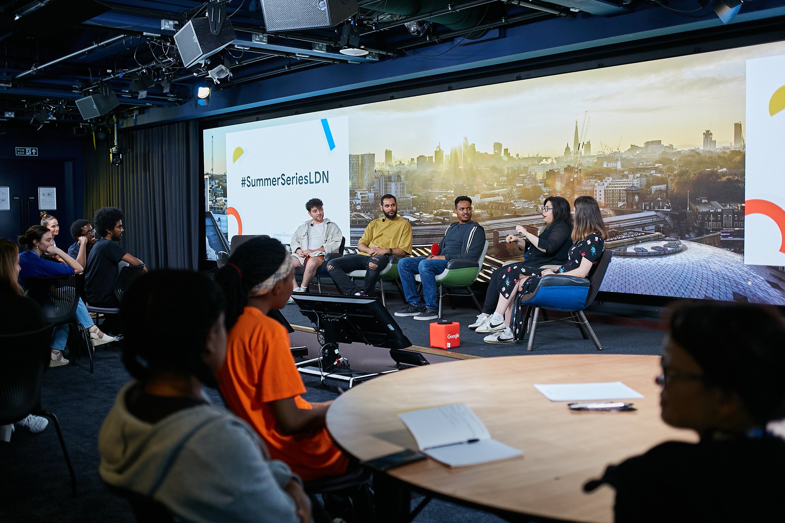 Panel discussion at #SummerSeriesLDN with audience attending, featuring a backdrop of a cityscape.