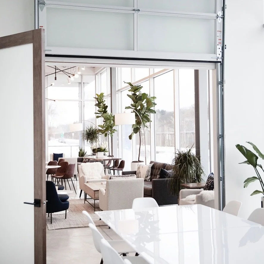 ModernWell Minneapolis's conference room and lounge area with large windows, variety of sofas and chairs, and tall indoor plants.
