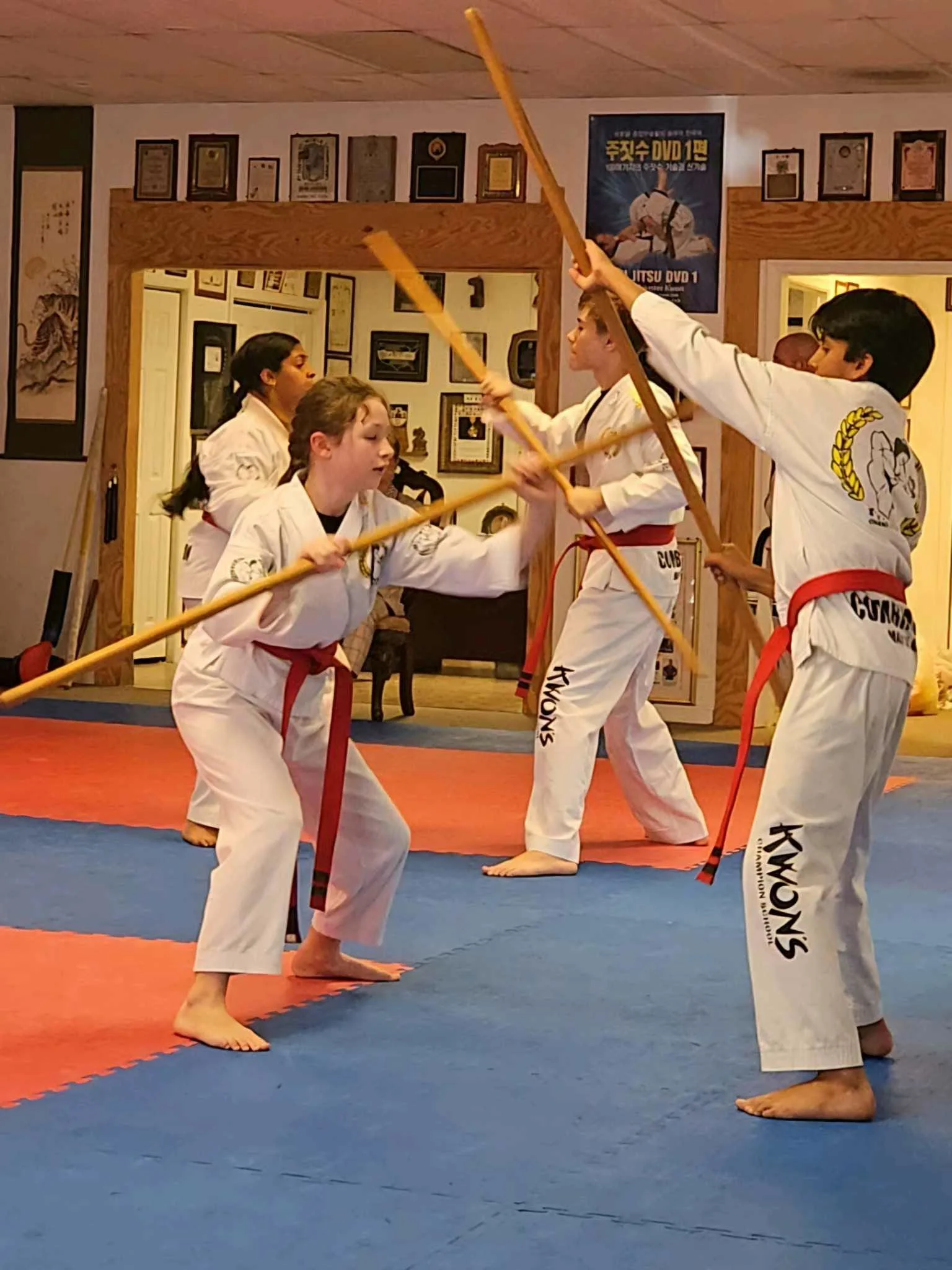 Karate students practicing in a dojo with martial arts posters and certificates on the wall.