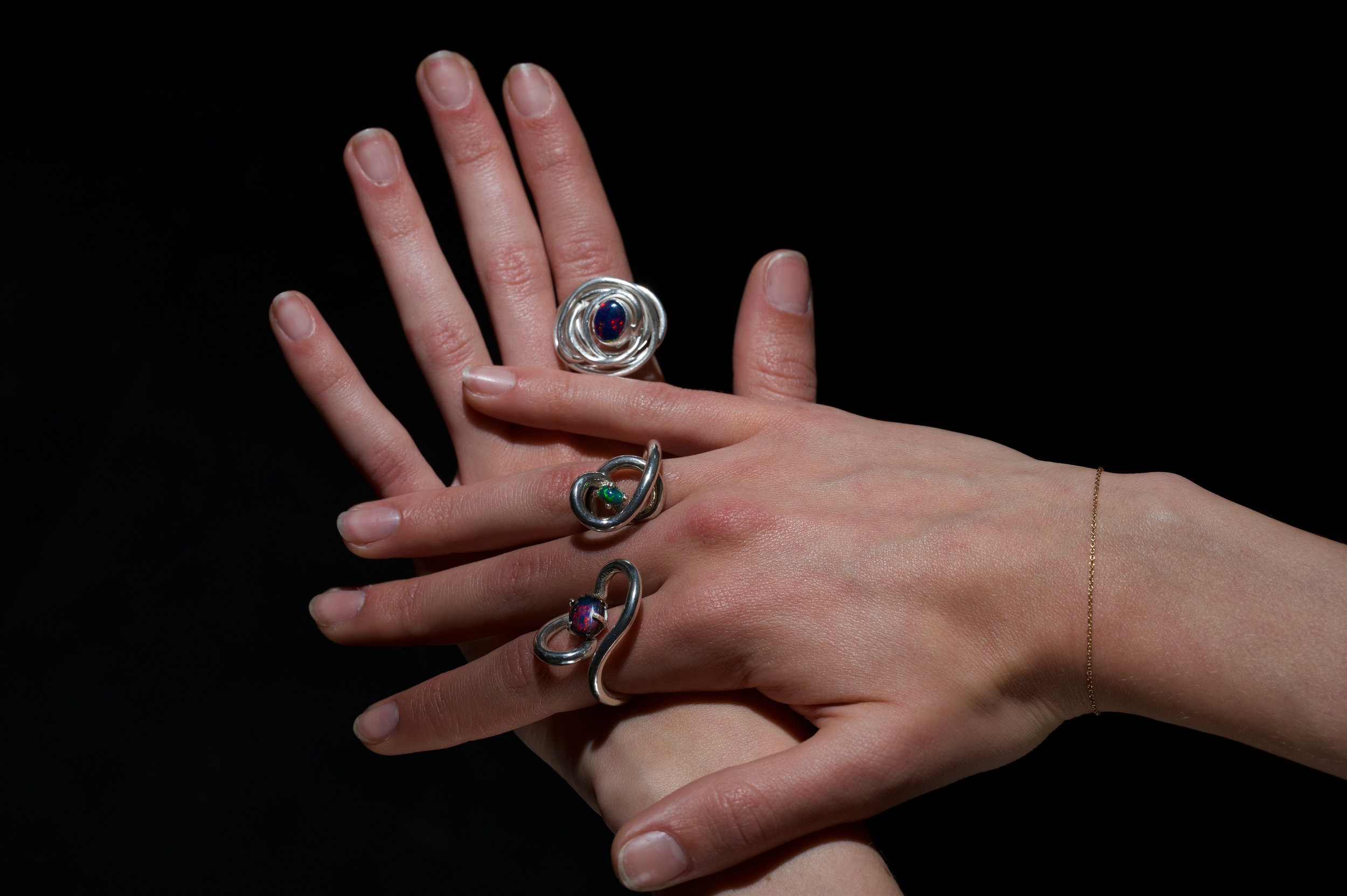 Multiple fingers adorned with silver rings, one featuring a dark red and blue gemstone, against a black background.