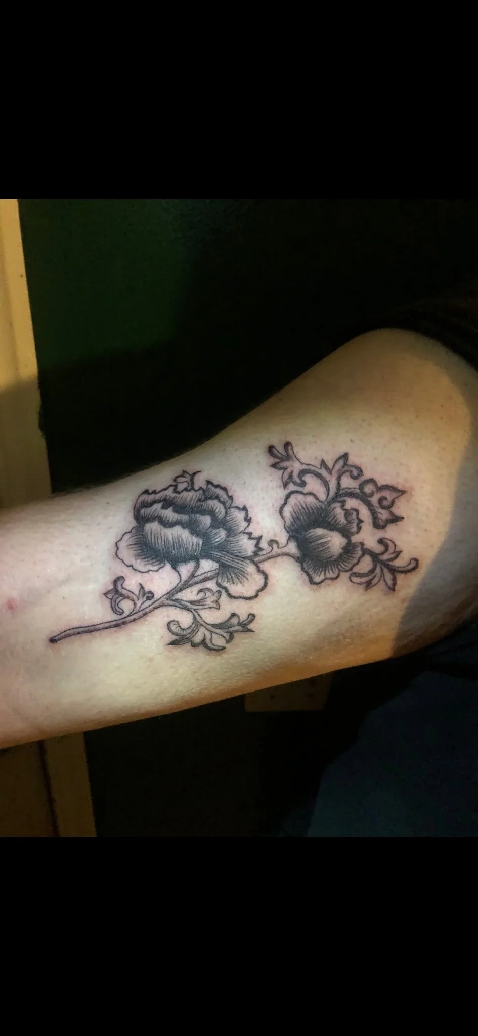 Black ink floral tattoo of two large flowers with leaves on a person's arm.