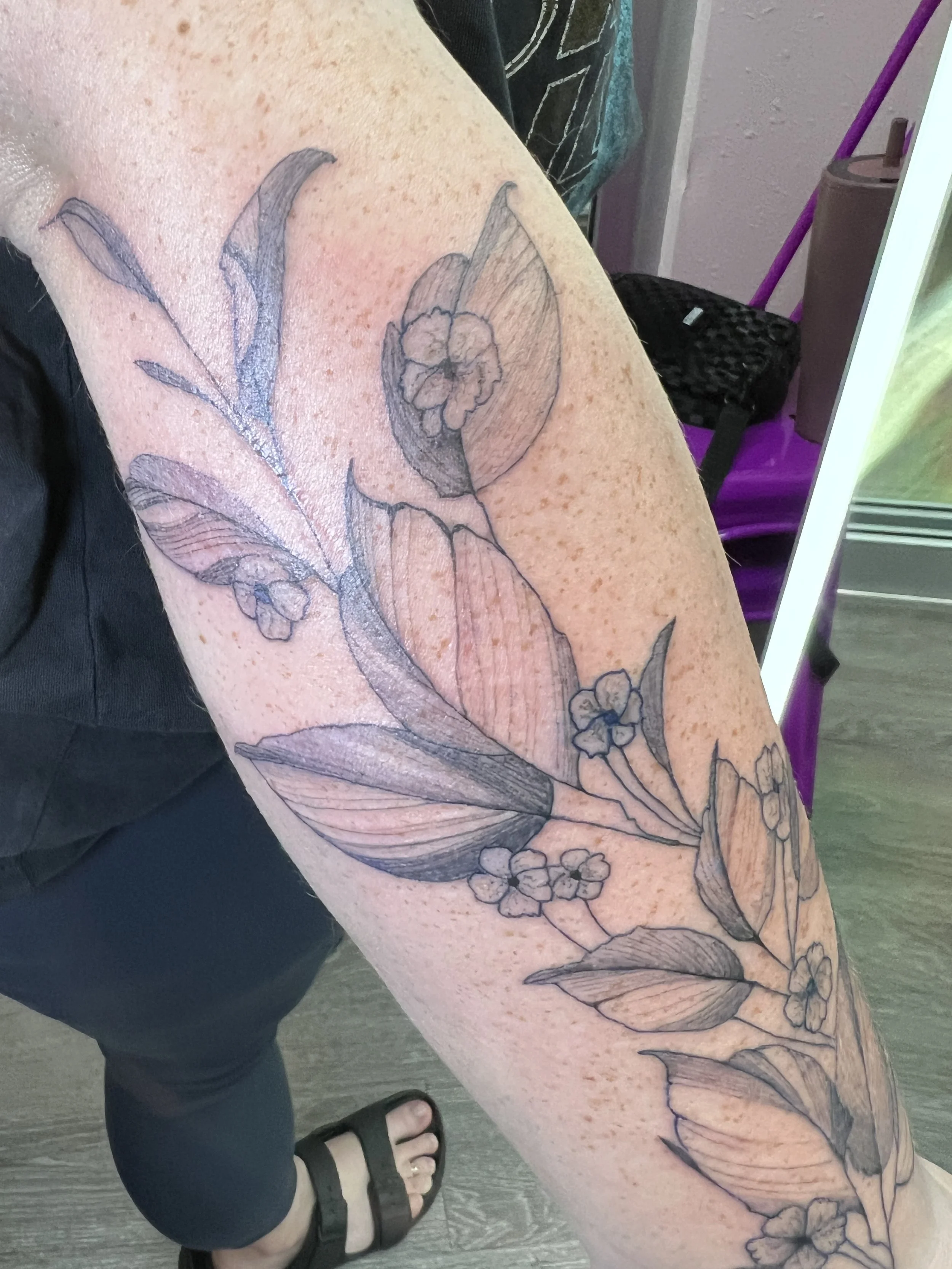 A person's arm with a floral tattoo featuring flowers and leaves.