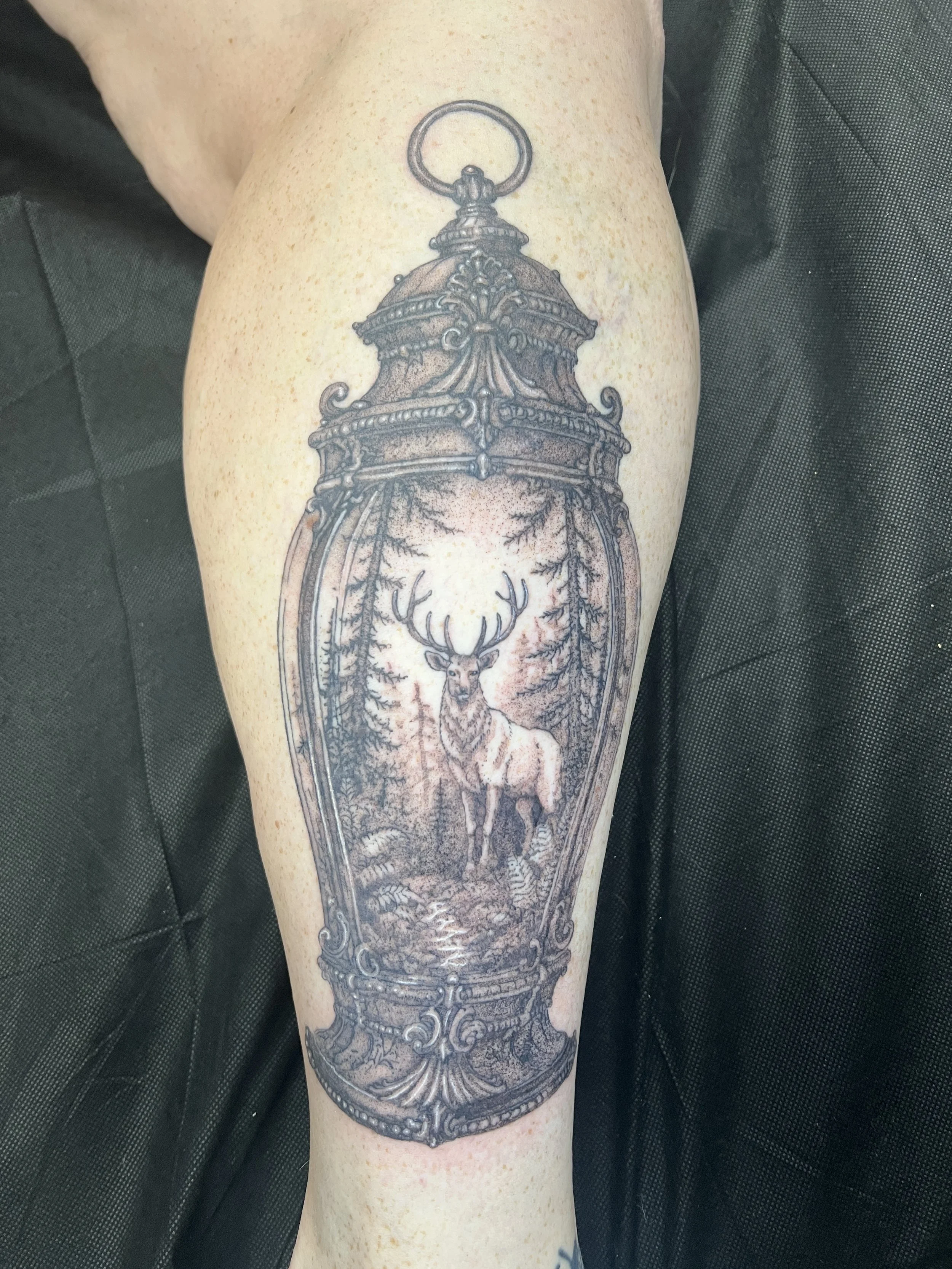 Tattoo of a deer inside an ornate mirror frame on a person's upper arm.