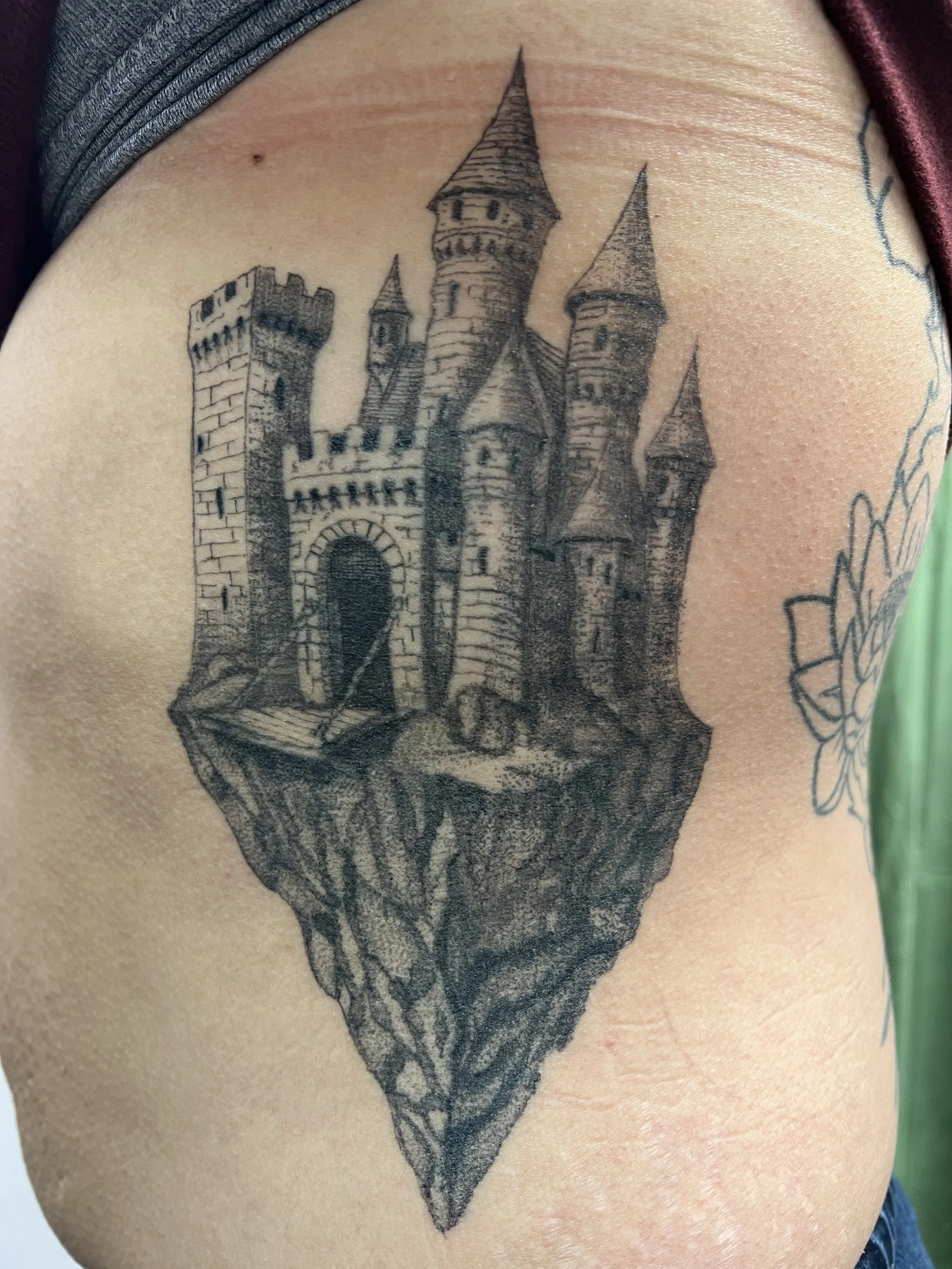 Black and gray tattoo of a detailed castle on a person's upper arm.