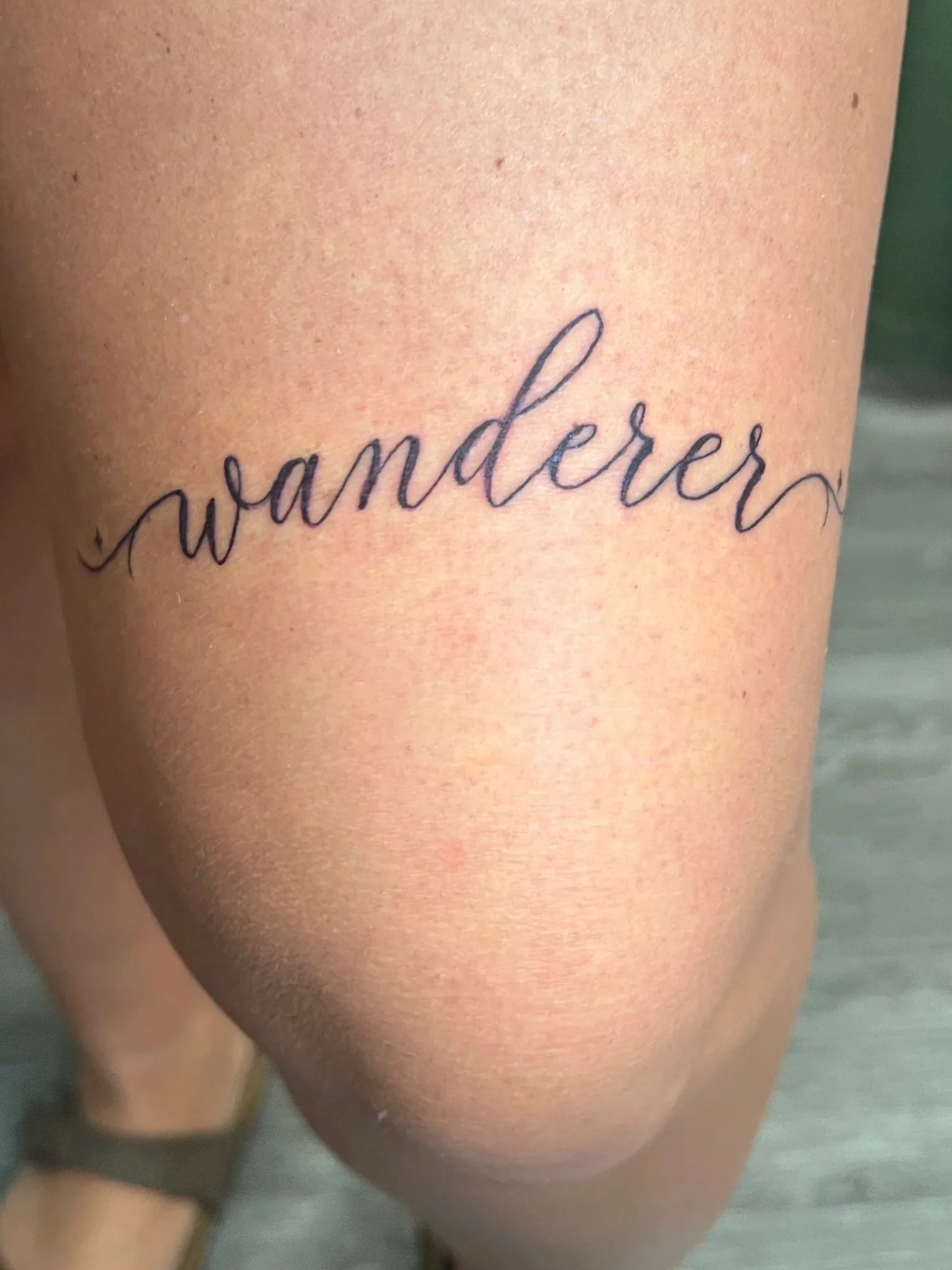Close-up of a person's skin with a tattoo that says 'wanderer' in cursive.
