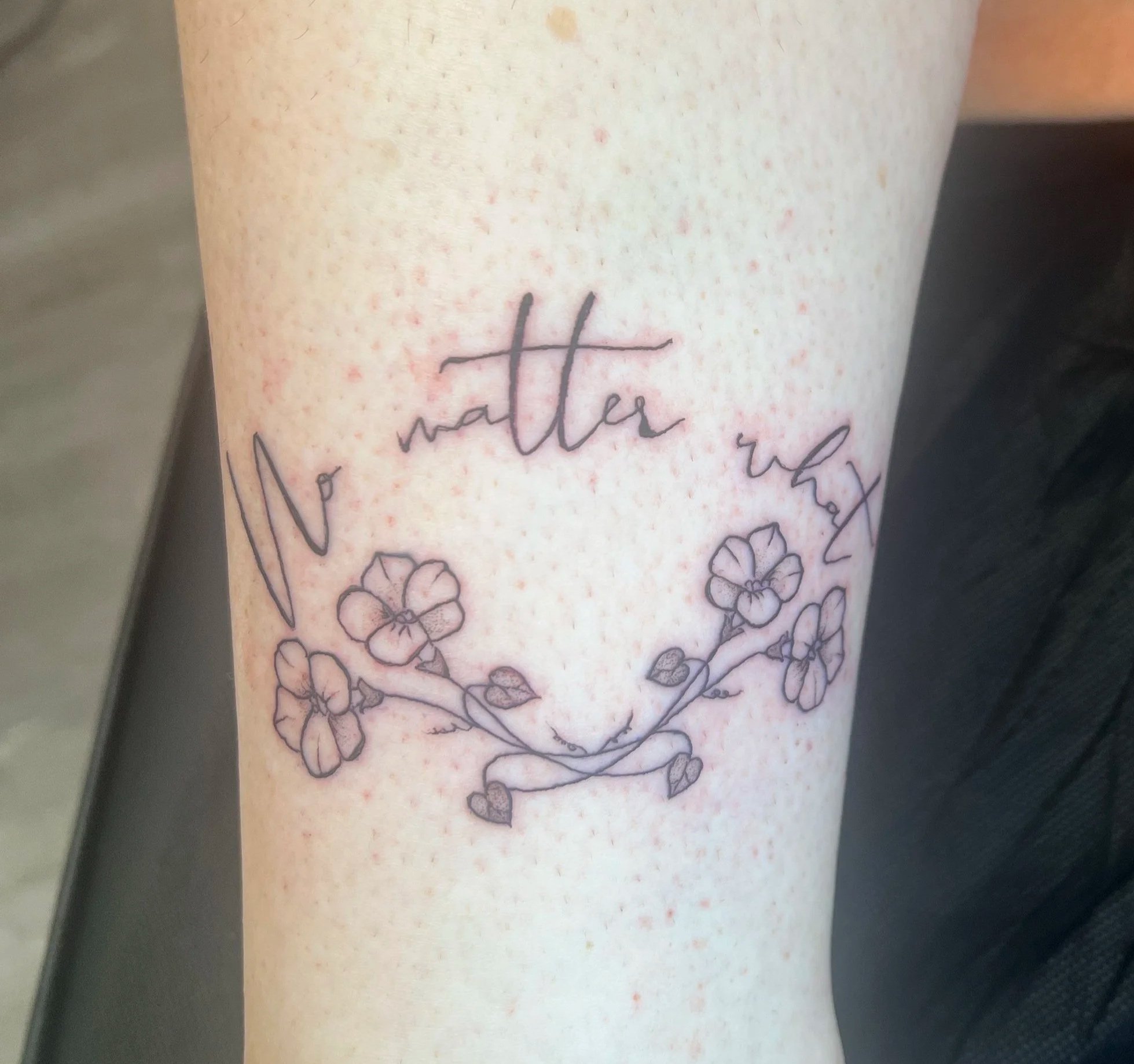 A person's arm with a fine line tattoo of the word 'water' and floral designs.
