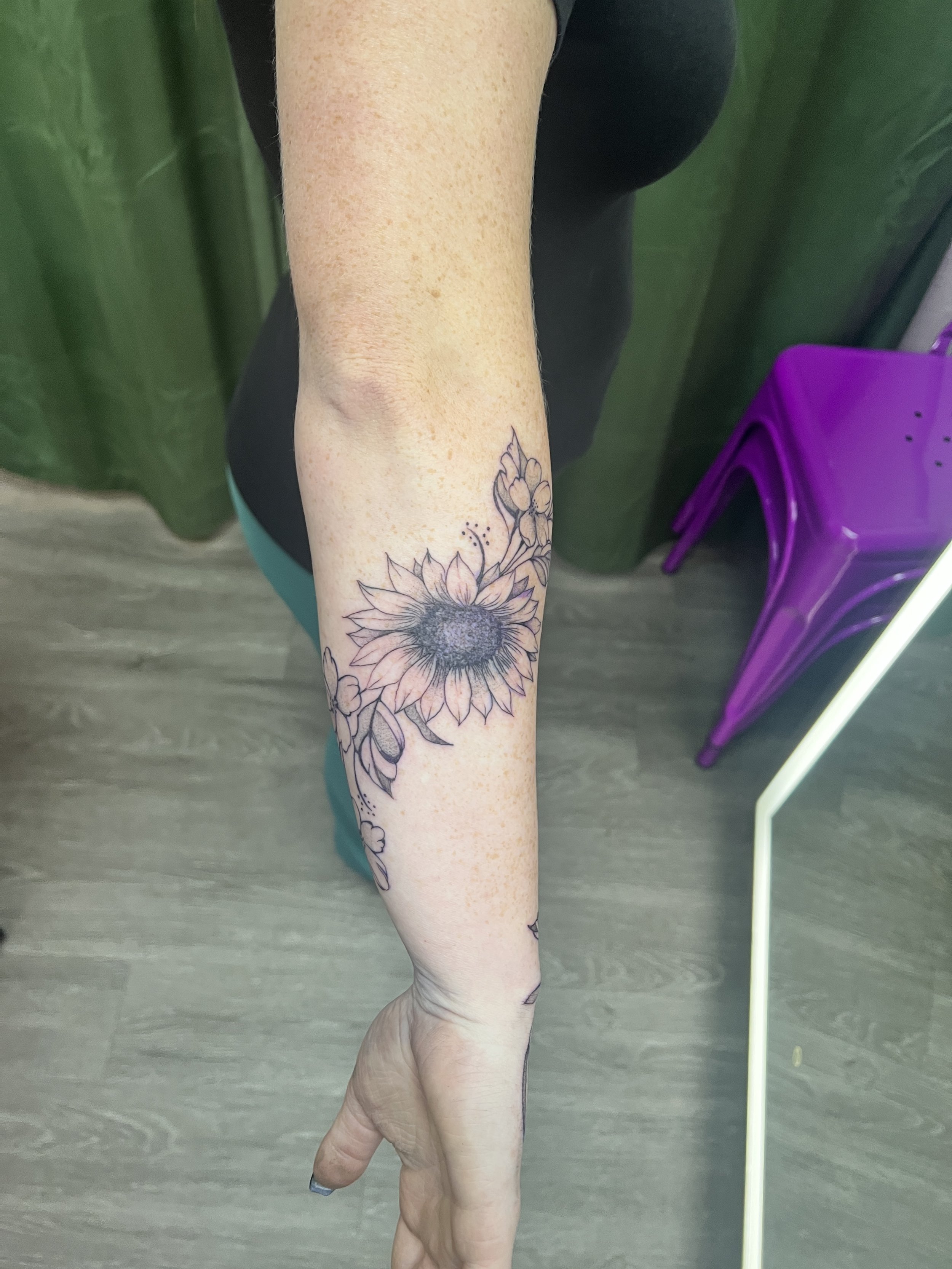 A person's arm with a sunflower tattoo on the forearm.