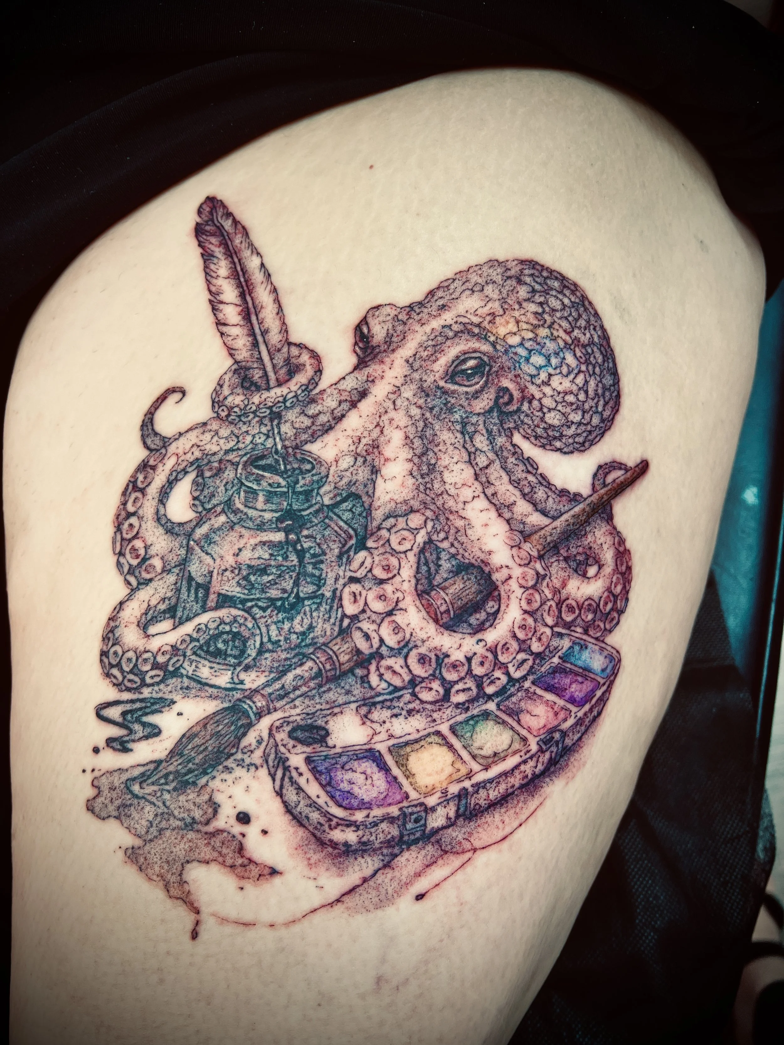 A colorful tattoo of an octopus holding a feather and a paintbrush on a person's upper arm.