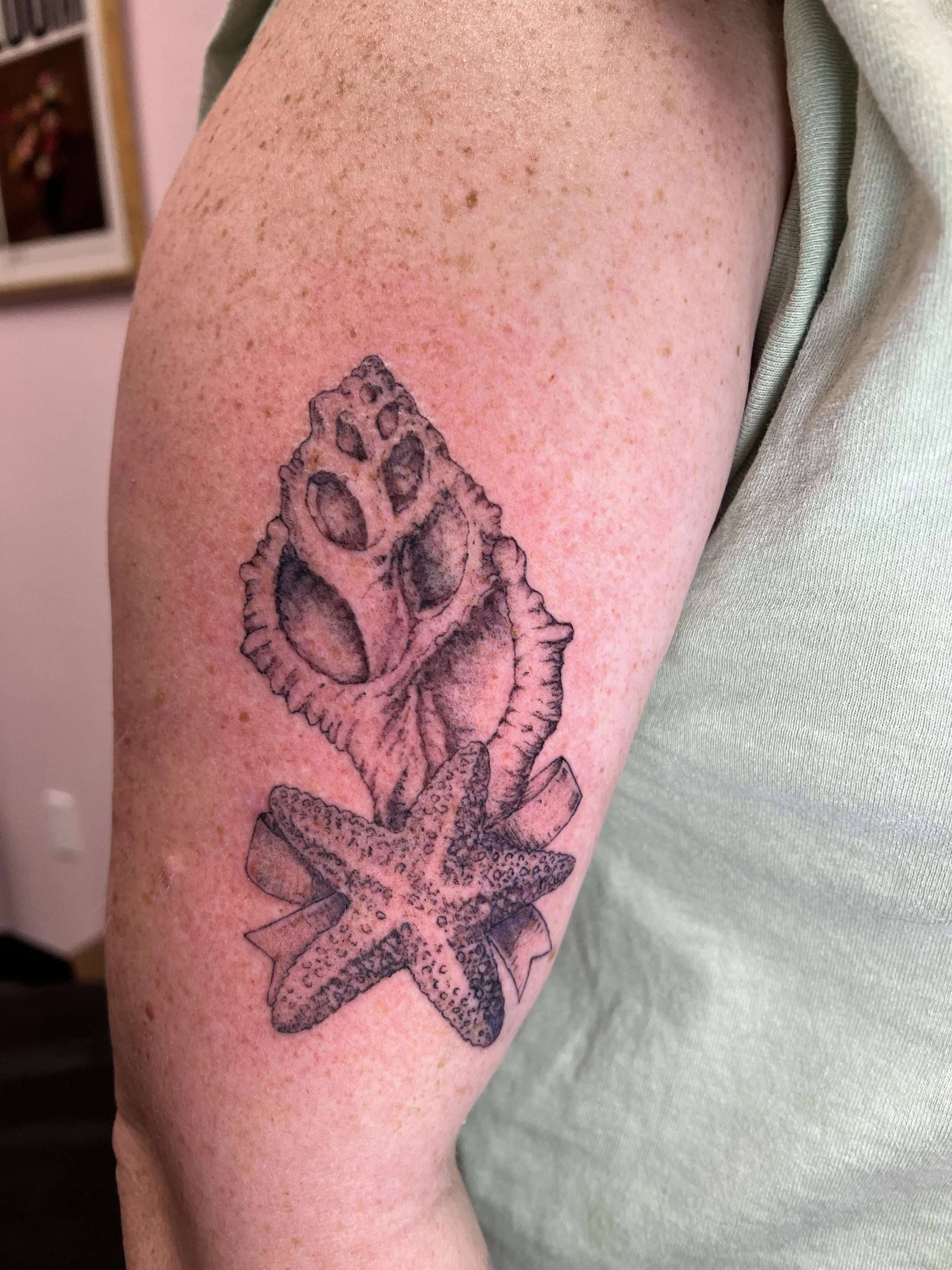 A tattoo of a condor skull with detailed shading on a person's upper arm, next to their green shirt and light-colored sleeve.