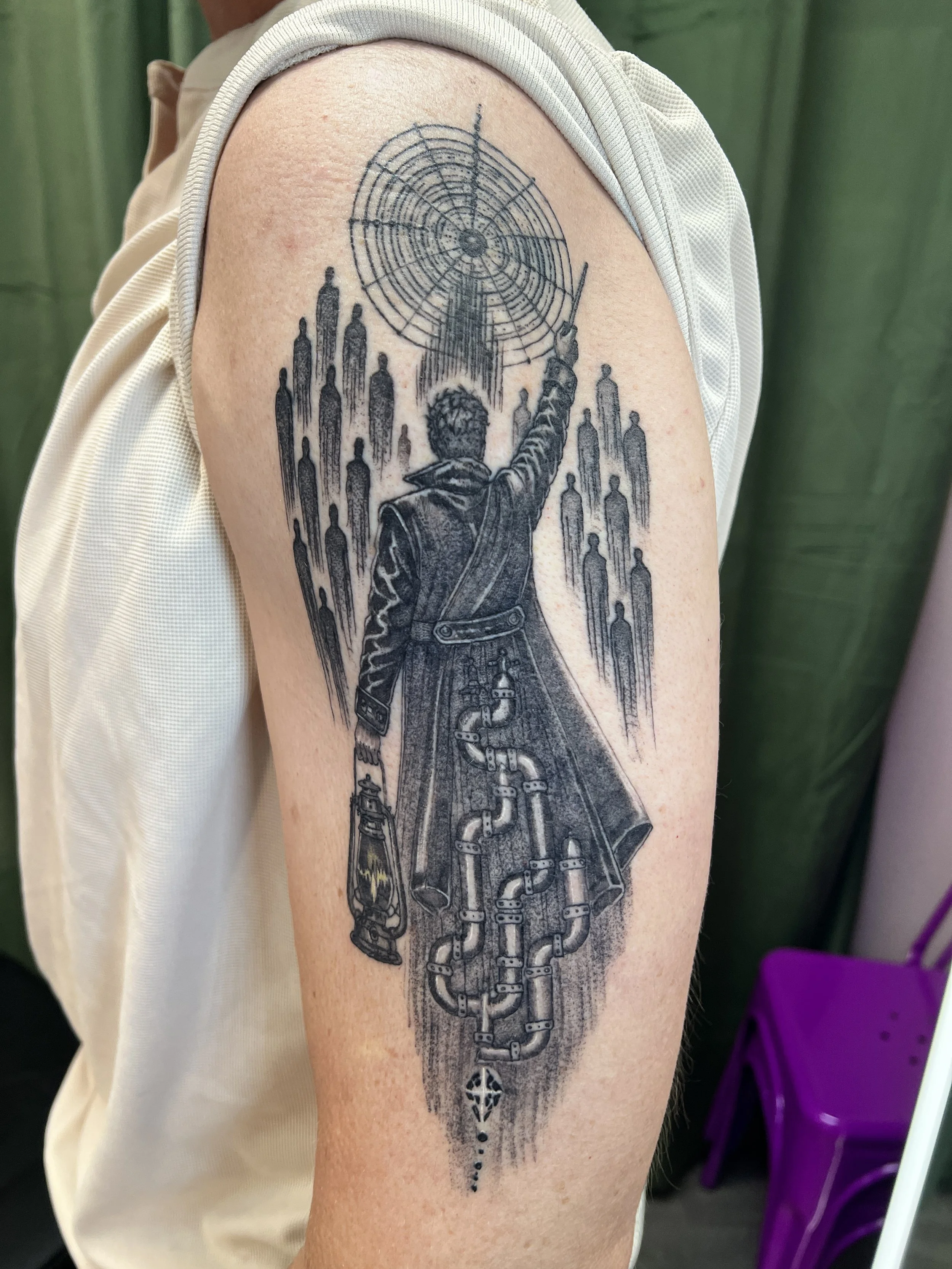A detailed black ink tattoo on a person's upper arm depicting a futuristic scene with a person in a coat reaching up towards a large, intricate spider web with various abstract and industrial elements and patterns.