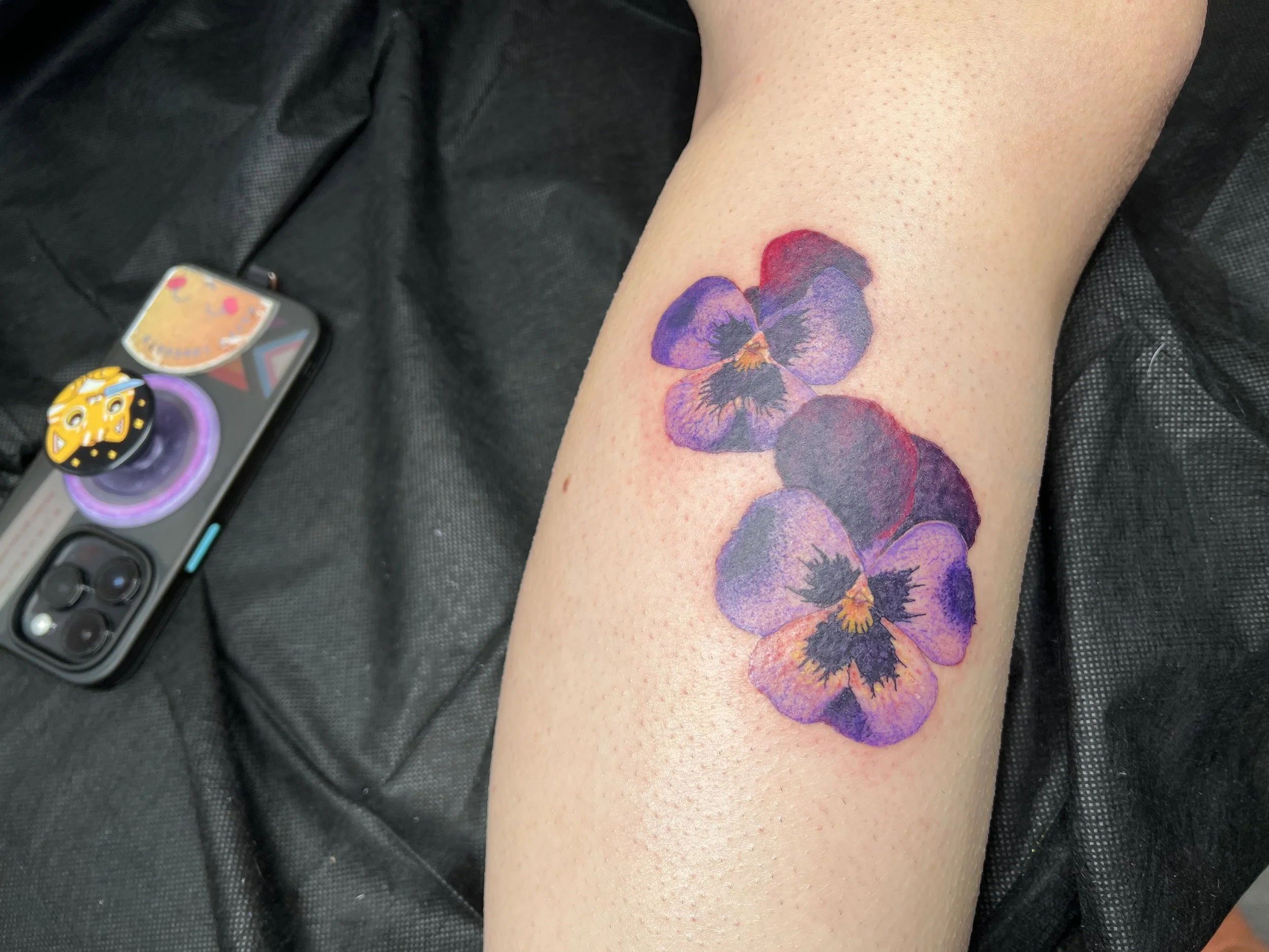 A colorful watercolor tattoo of purple and red violets on a person's forearm.