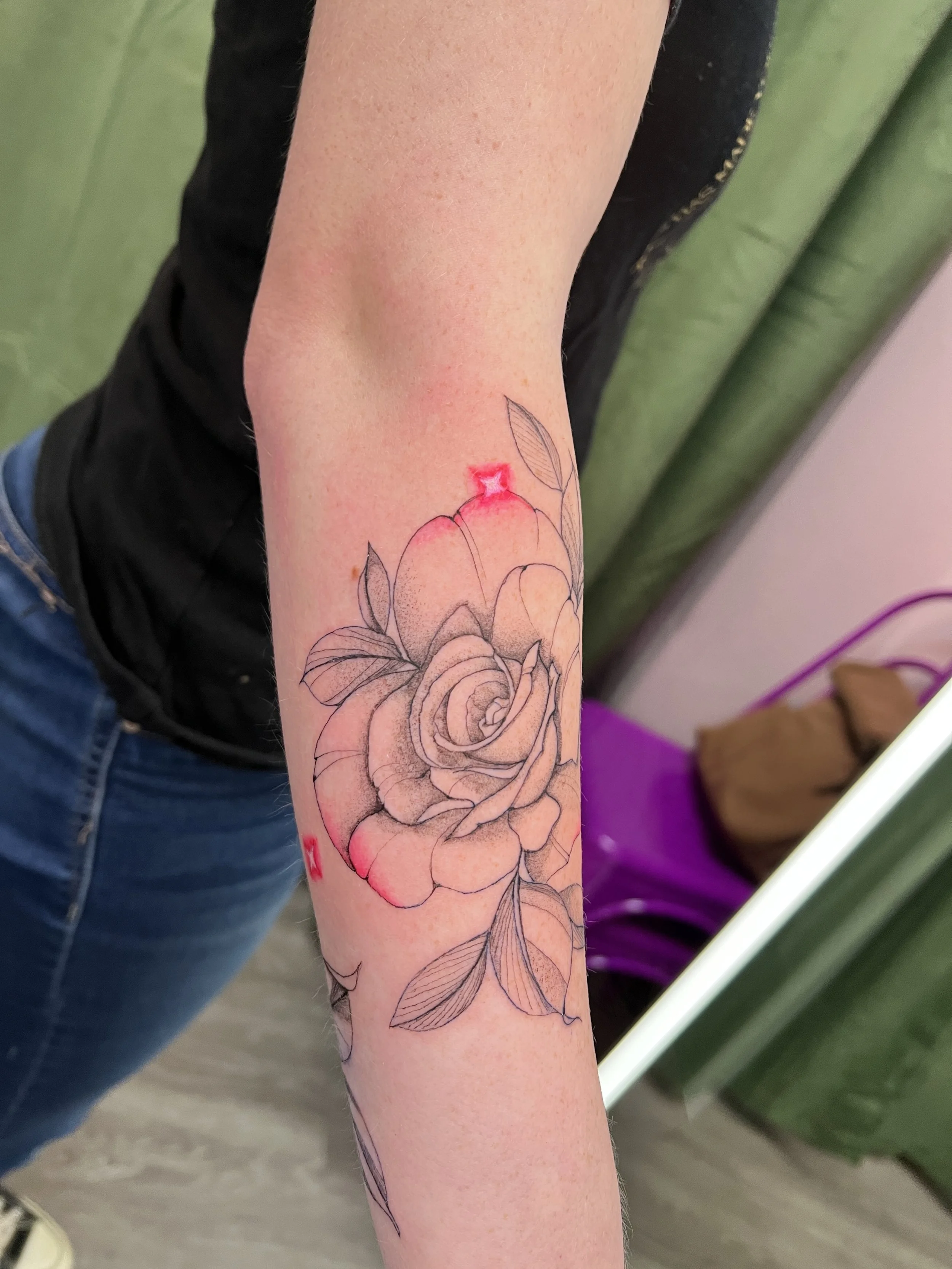 A person's forearm with a floral tattoo fine line, and red highlights on the upper part of the tattoo.