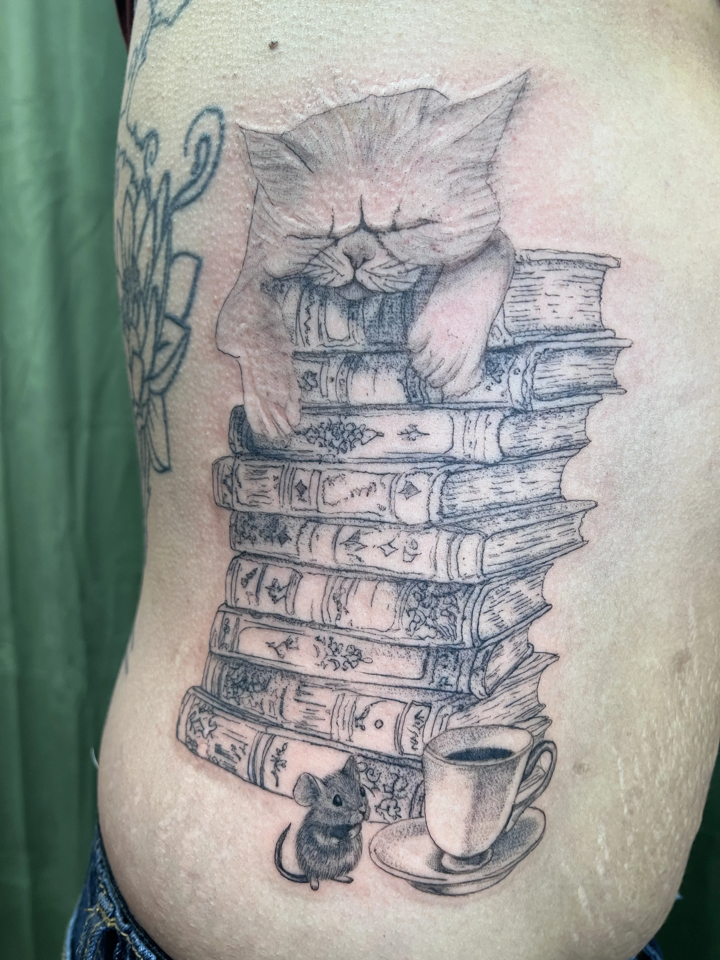Tattoo of a cat sleeping on a stack of books with a paw print and a mouse nearby.