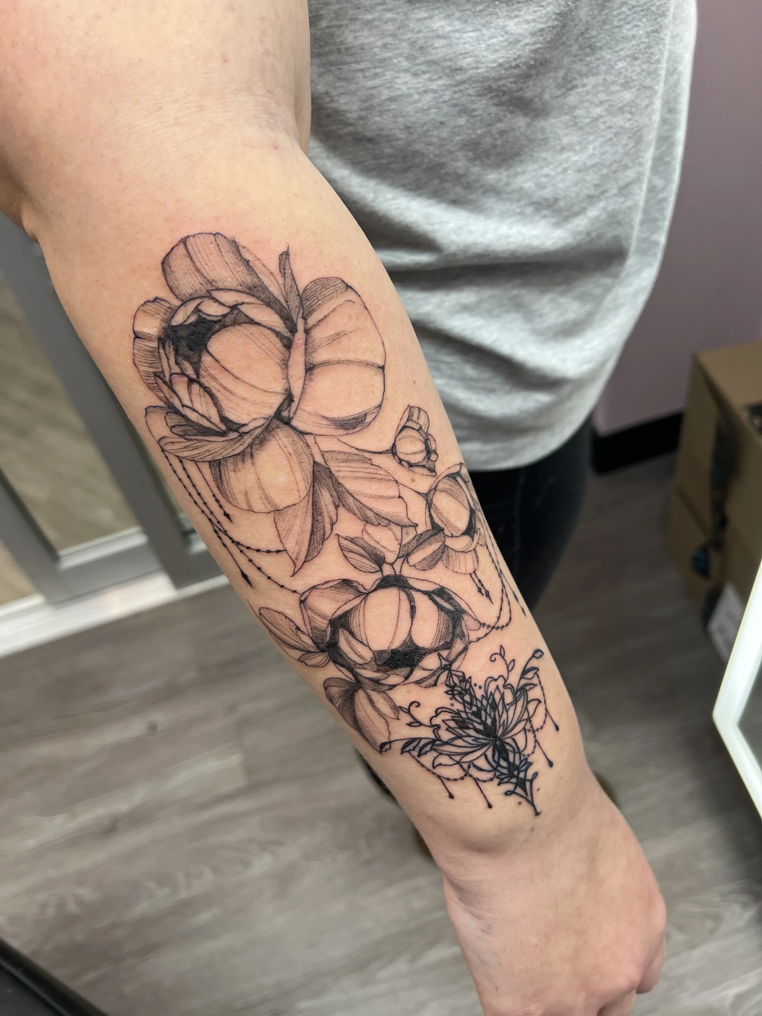 Black outline floral tattoo on person's forearm.