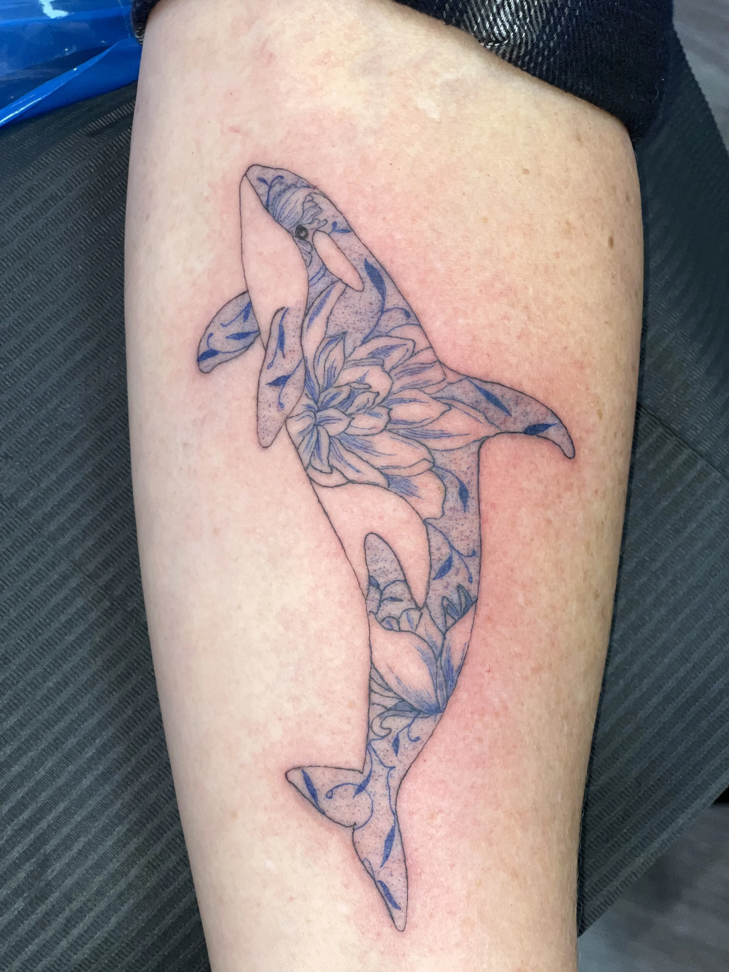 Tattoo of a dolphin with floral patterns on its body on person's upper arm.