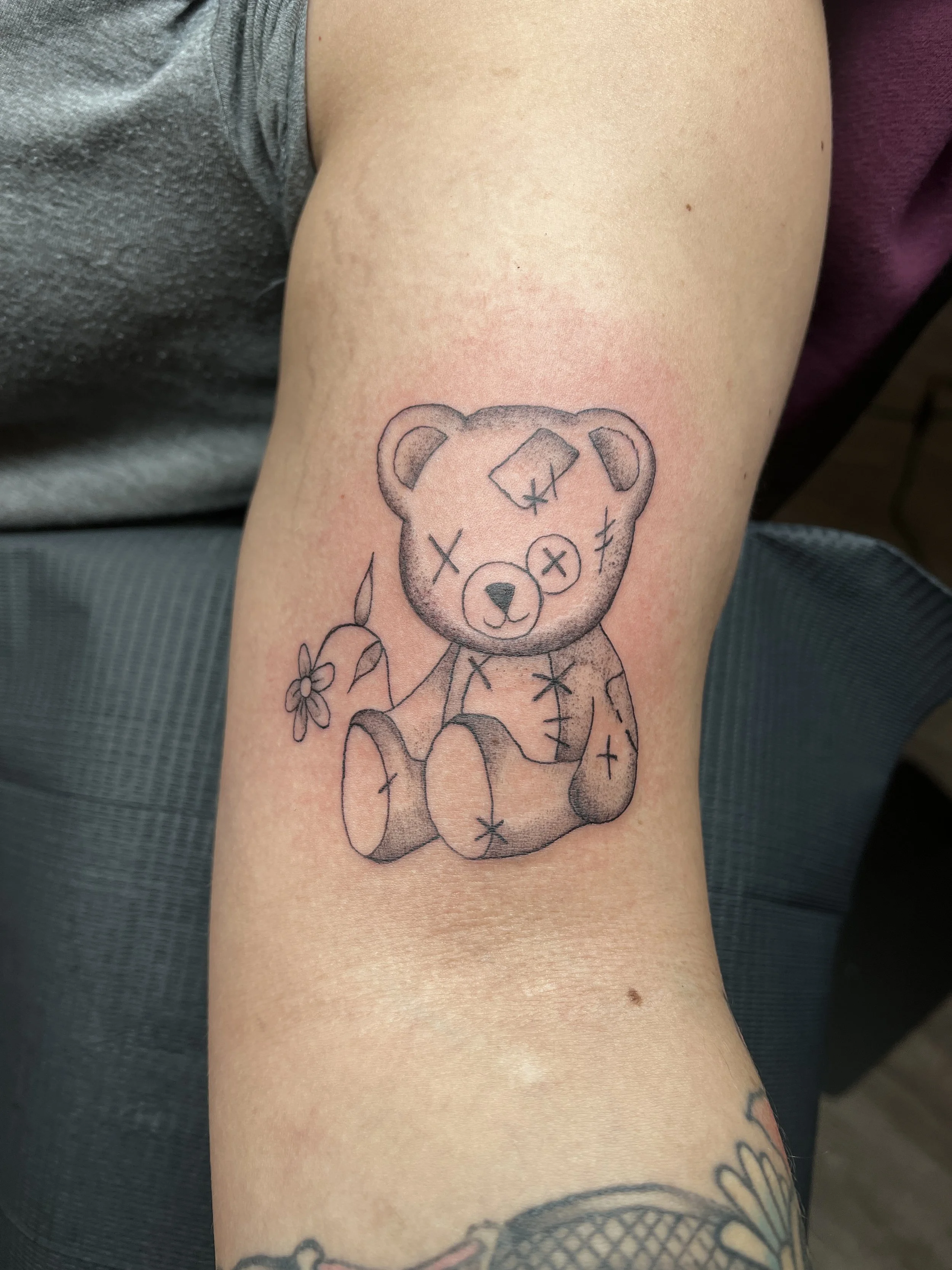 Tattoo of a teddy bear holding a flower on a person's arm.