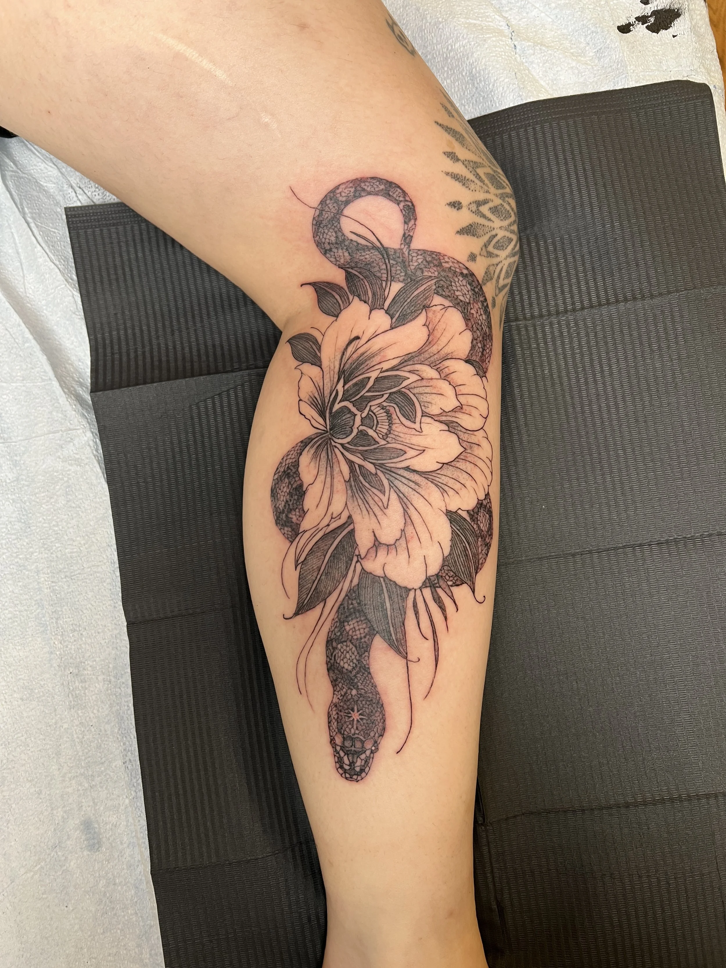 A tattoo of a snake intertwined with a large peach-colored flower on a person's leg.