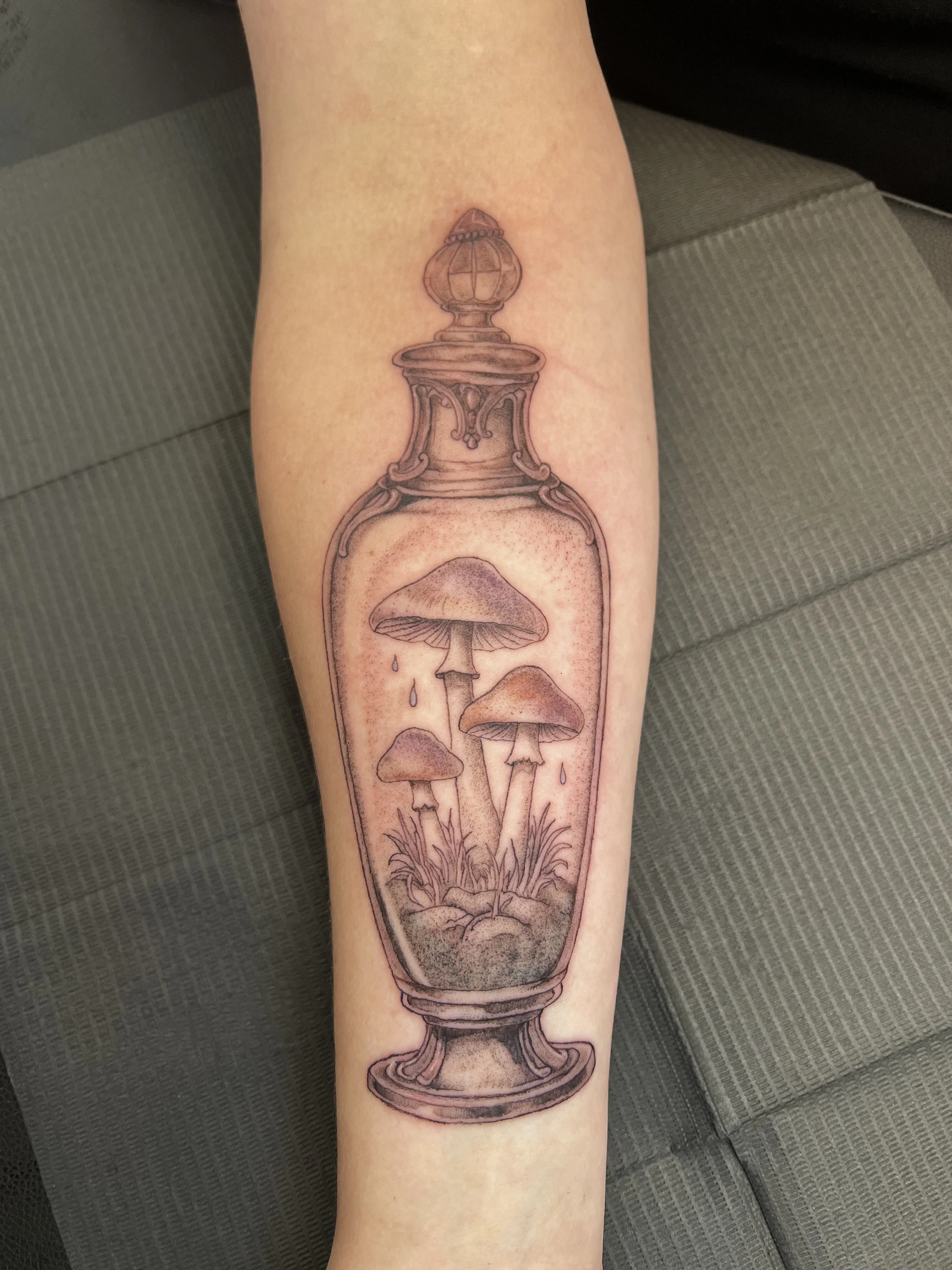 Fine line tattoo of a cup with mushrooms inside, with mushrooms growing at the bottom and drops falling.
