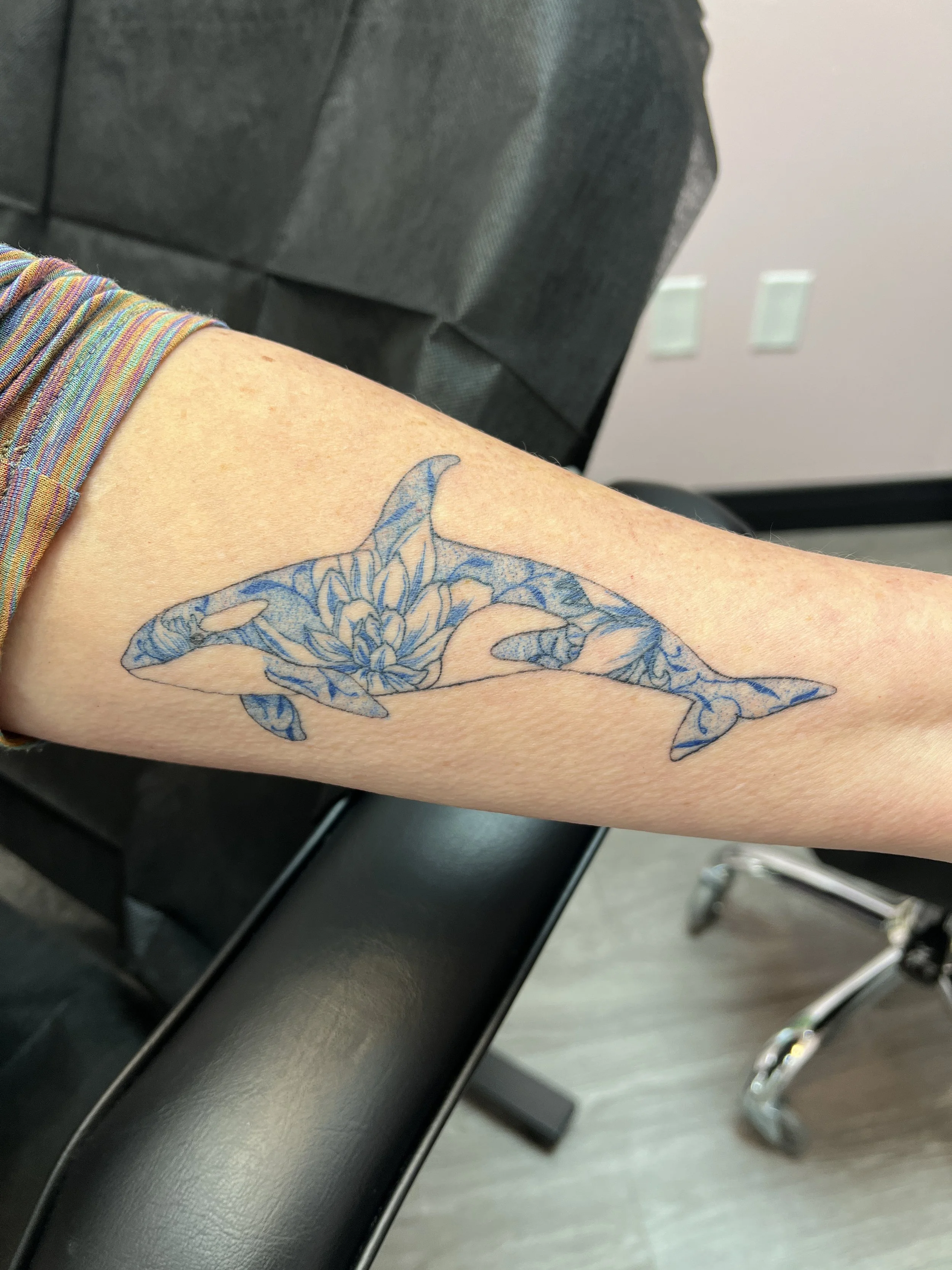 Close-up of a person's arm with a tattoo of a whale on it, the person is sitting in a waiting room chair.