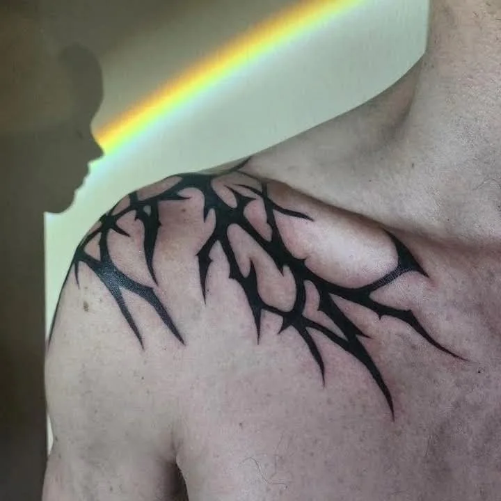 Close-up of a shoulder with a black tribal tattoo, with a  rainbow projecting onto it and a person's face silhouette in the background.