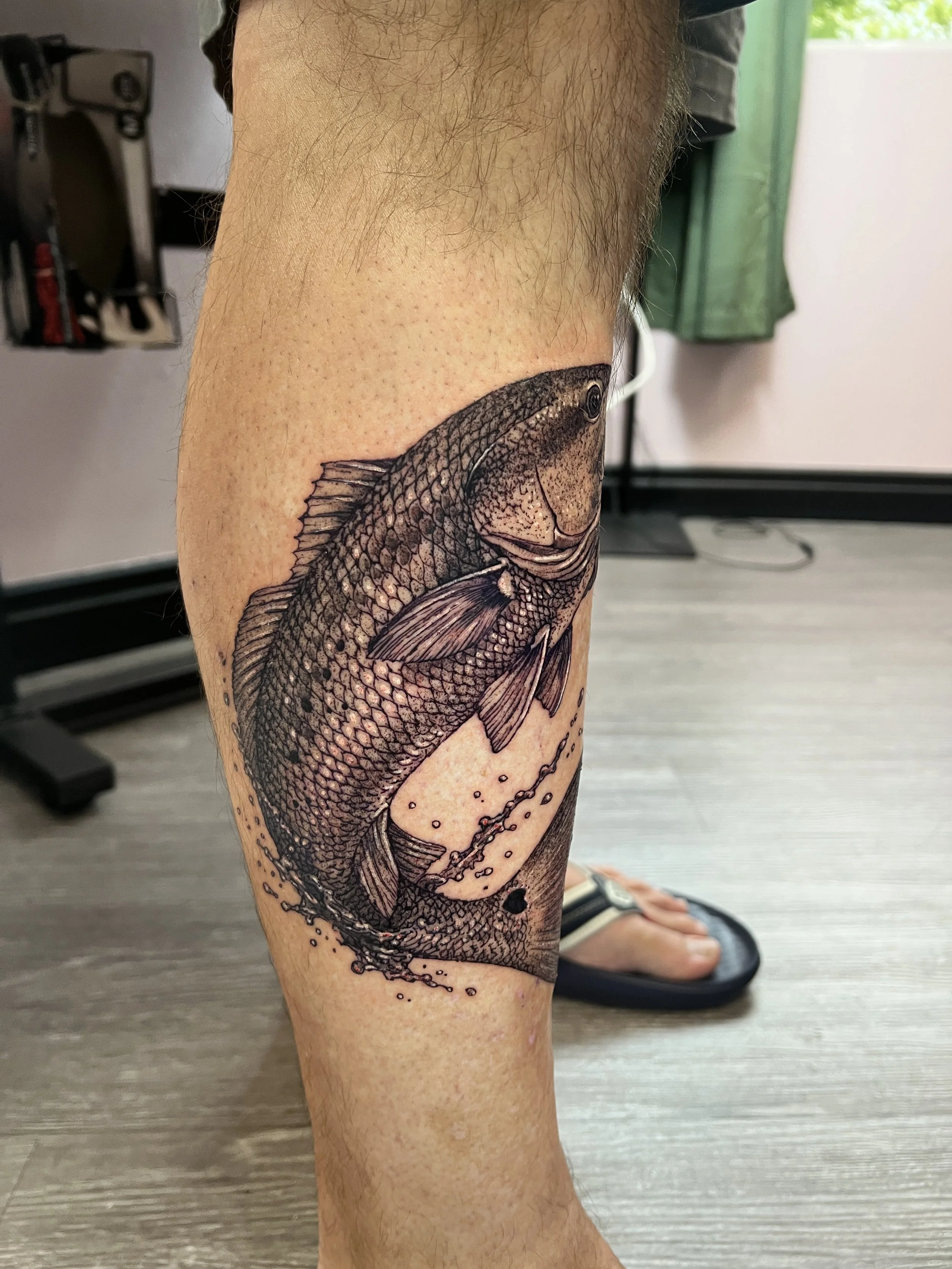 A detailed black and gray tattoo of a fish covering most of a person's thigh.